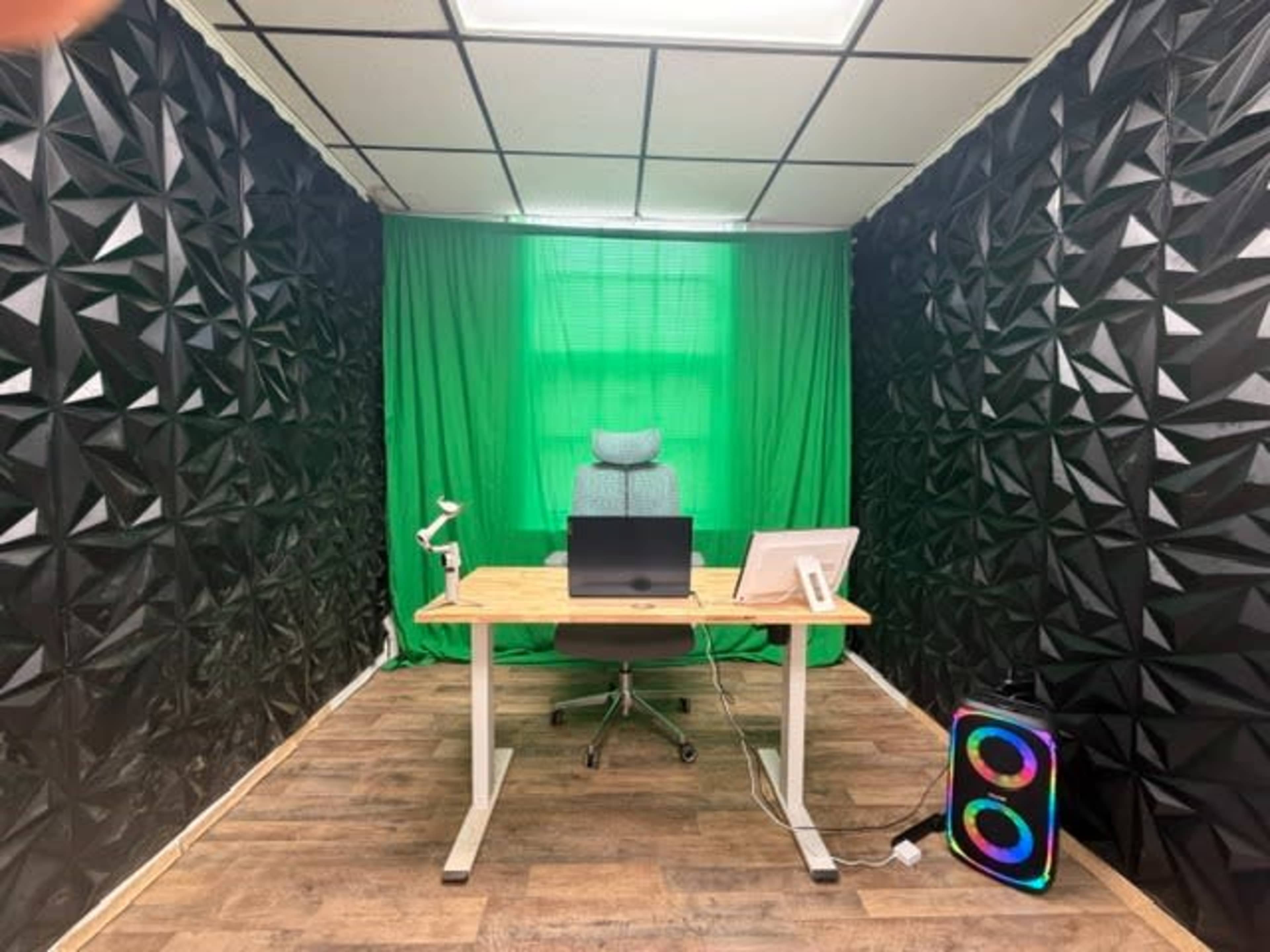 The image shows a modern office space featuring a desk with a computer, a chair, and large green curtains, surrounded by textured black walls.