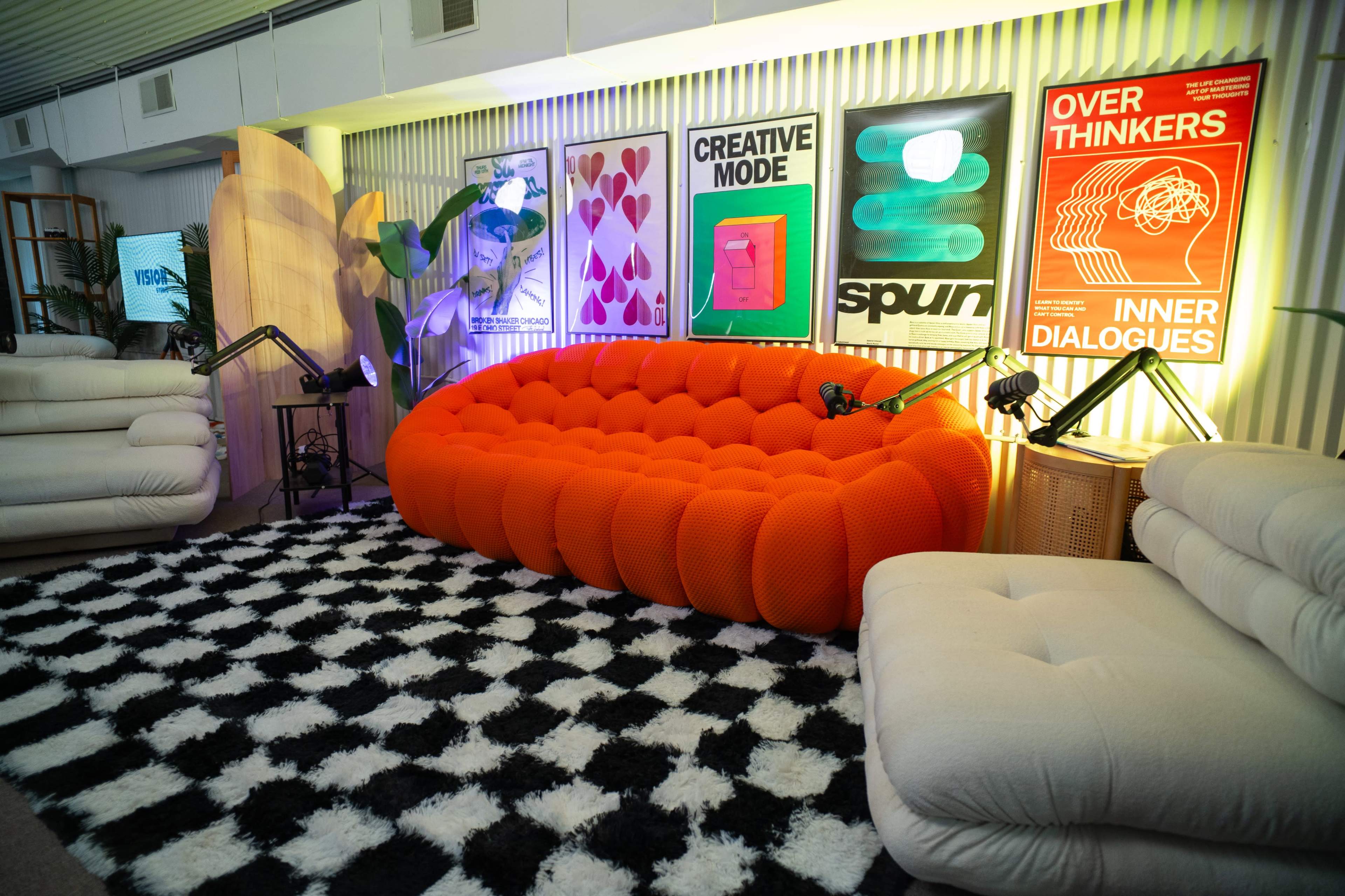 The scene features a vibrant orange bubble sofa set against a backdrop of textured walls adorned with modern, colorful prints, alongside a black and white patterned rug.