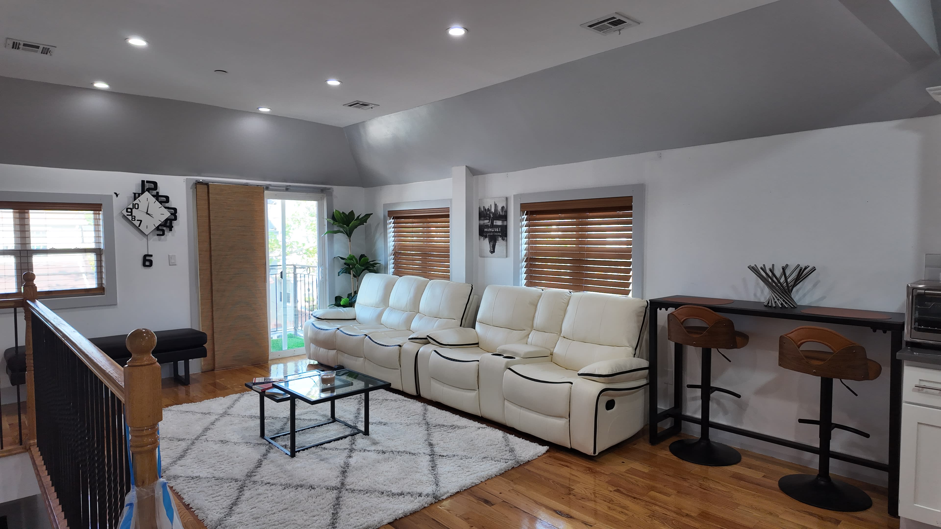 A modern living room features a white sectional sofa, a glass coffee table, and wooden flooring with large windows allowing natural light.