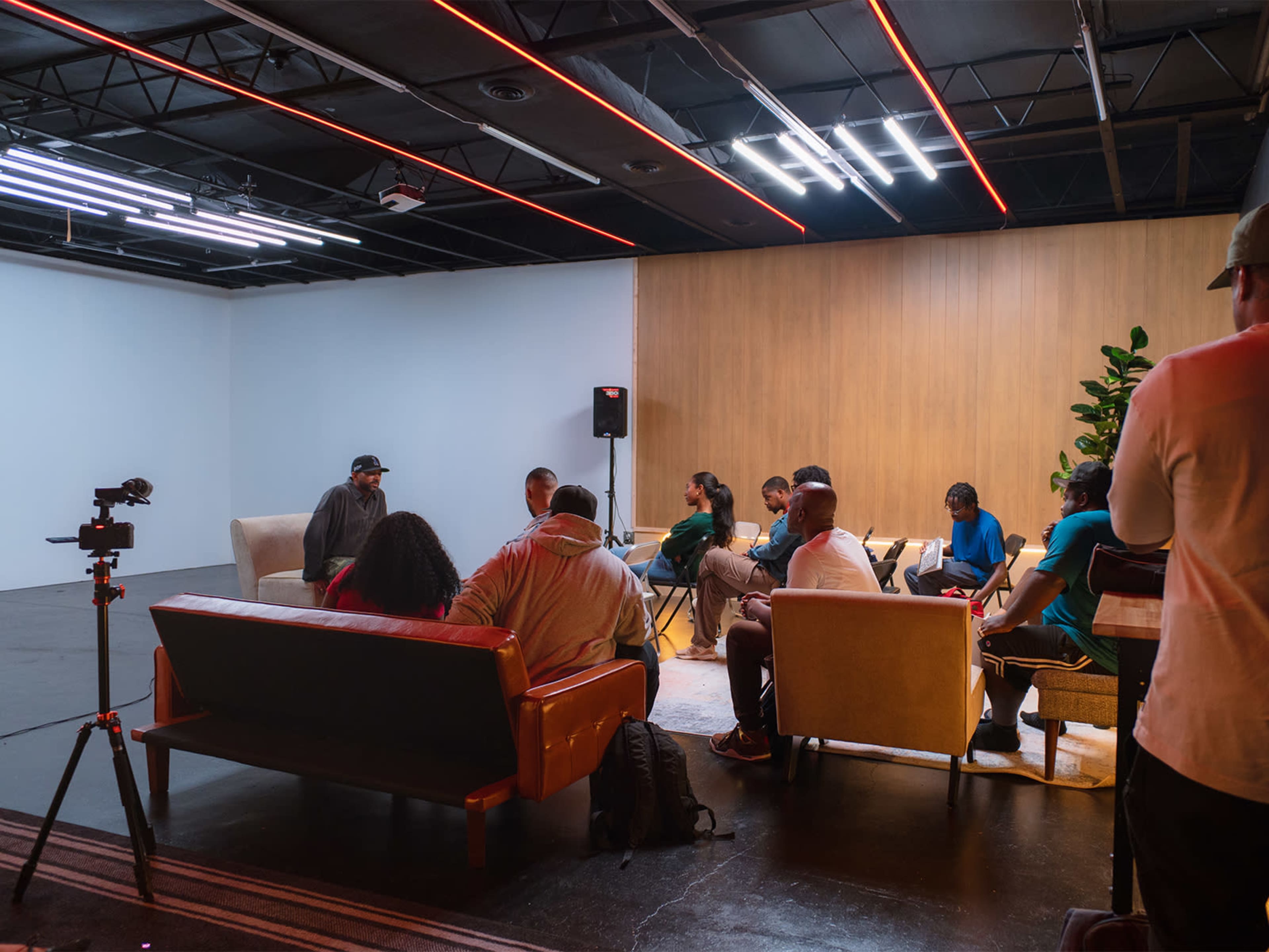 A group of people is engaged in discussion in a spacious, well-lit room with modern furniture and a wooden accent wall.