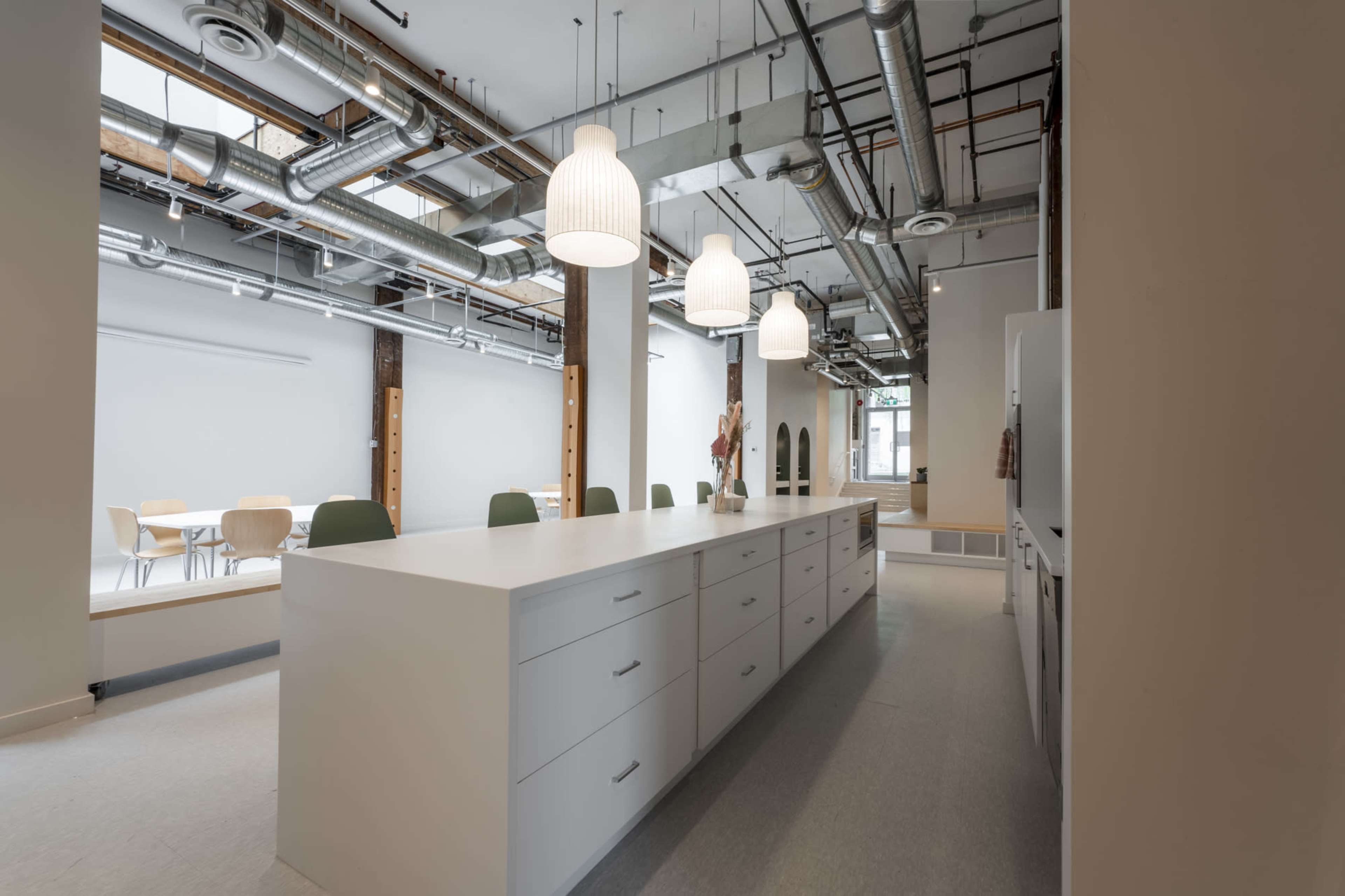 A modern kitchen with a large white island, overhead pendant lights, and exposed ductwork in an open space.