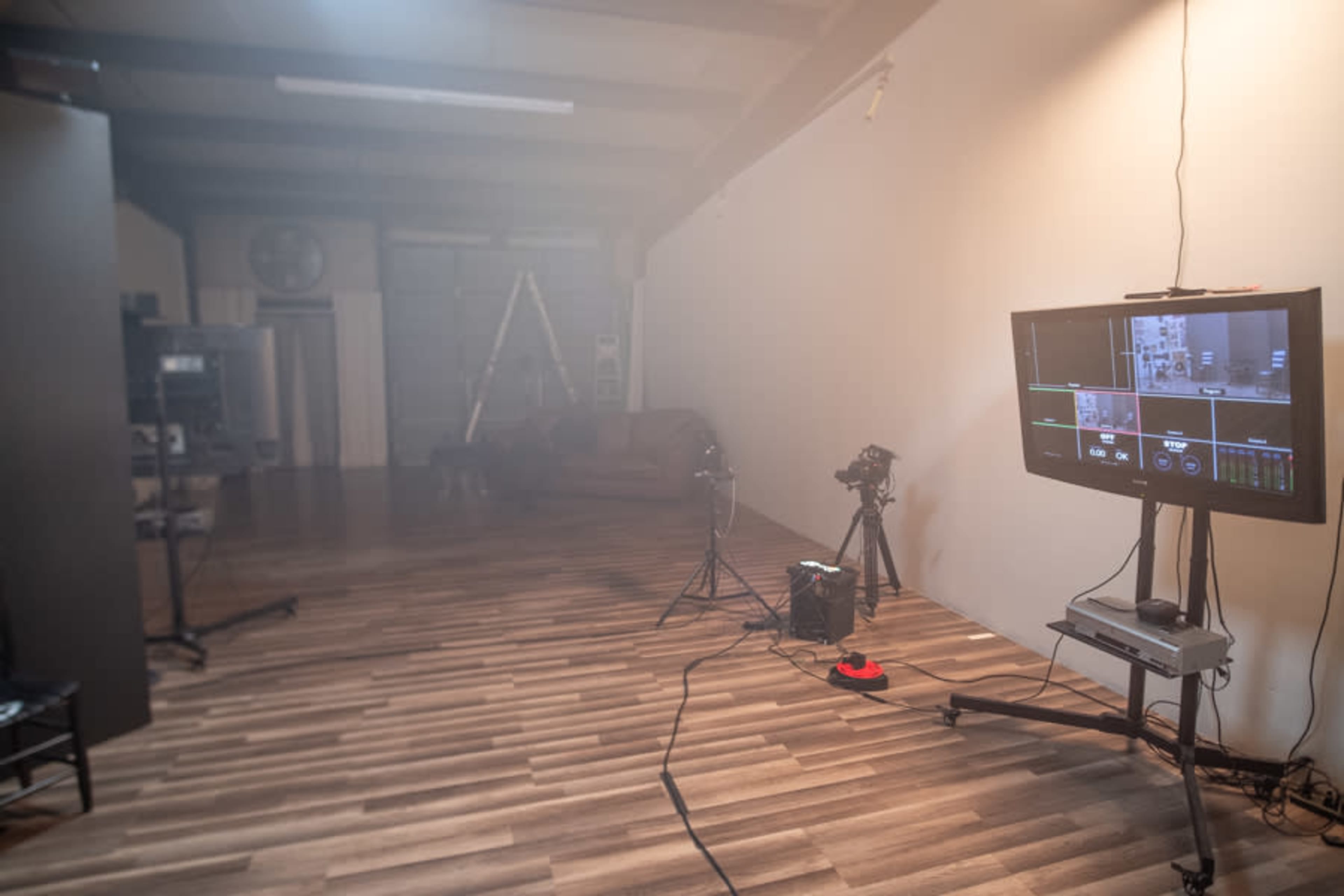 A minimalistic studio space with wooden flooring, a monitor displaying a control interface, and several cameras positioned around the room.