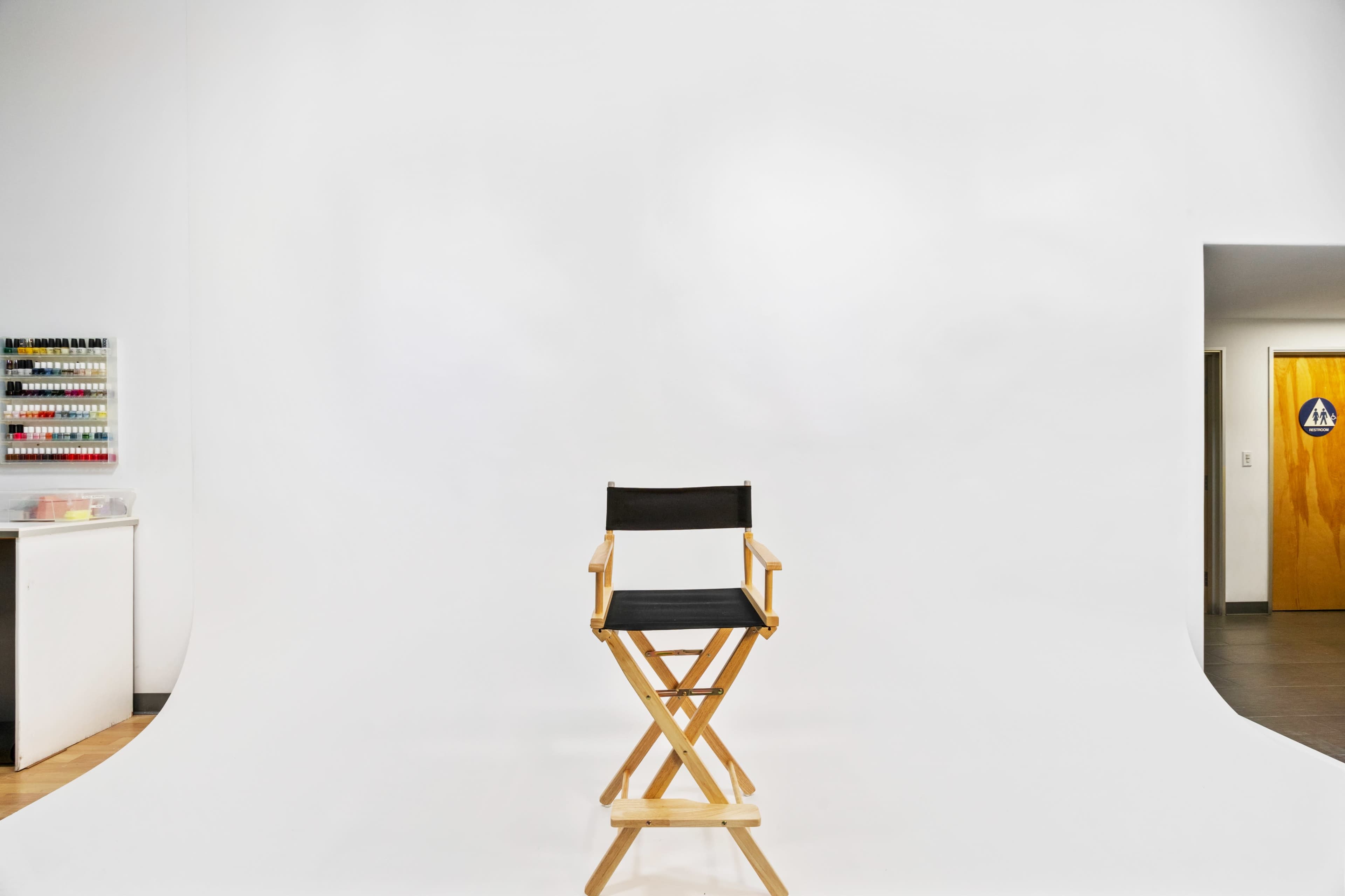 A wooden director's chair is positioned in front of a plain white backdrop in a studio space.