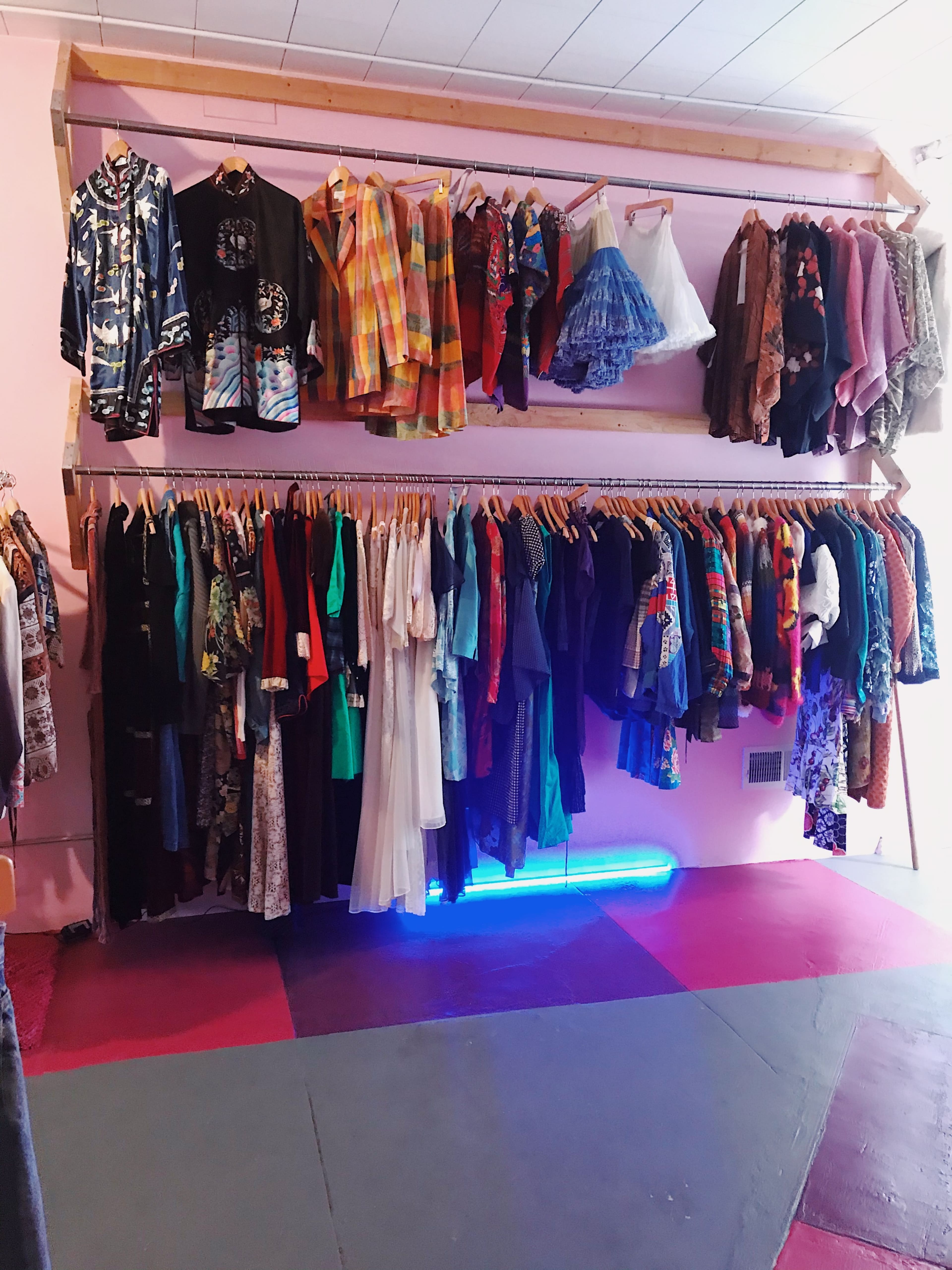 A boutique with two clothing racks displaying a variety of colorful garments, including dresses and jackets, against a pink wall.