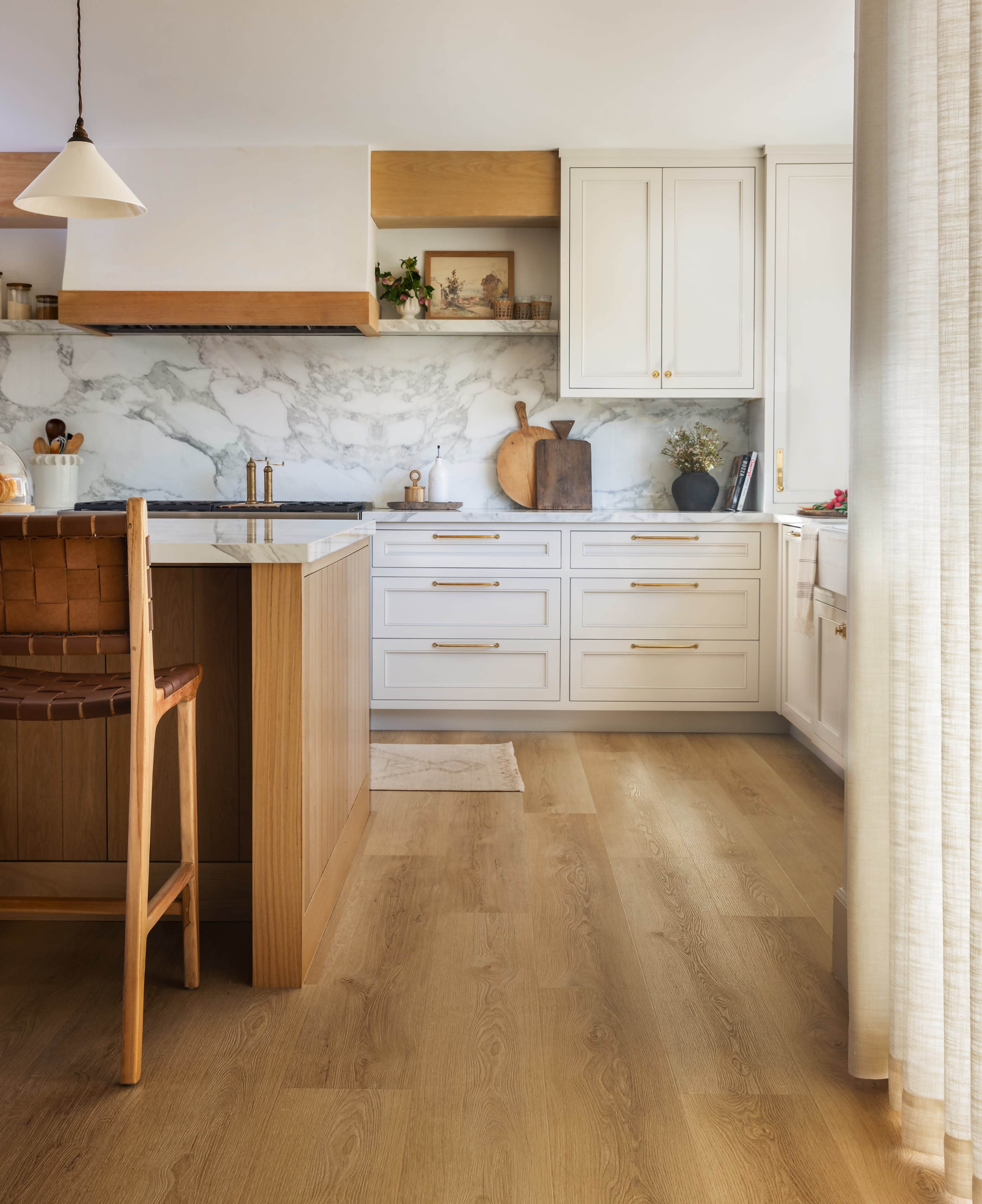 A modern kitchen features white cabinetry, a marble backsplash, and wooden accents, with a bar stool positioned at the island.