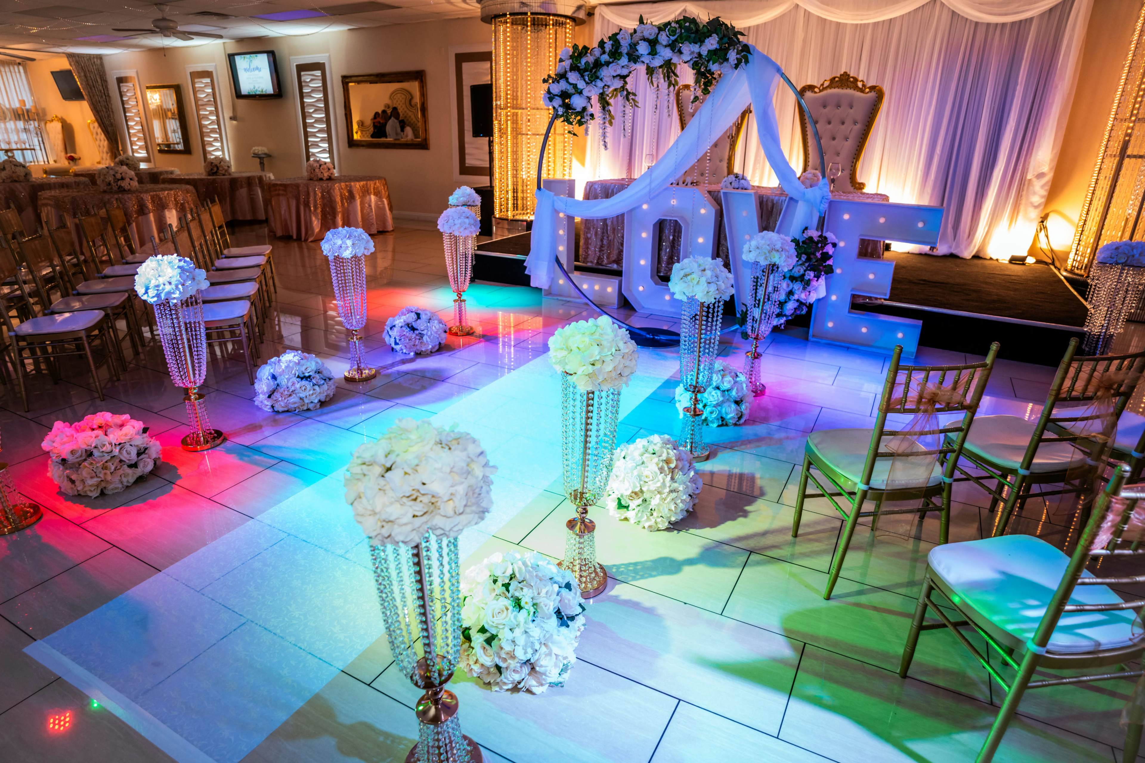 The image shows a wedding ceremony setup featuring large letters spelling "LOVE," floral arrangements, and elegant seating under a decorated archway.