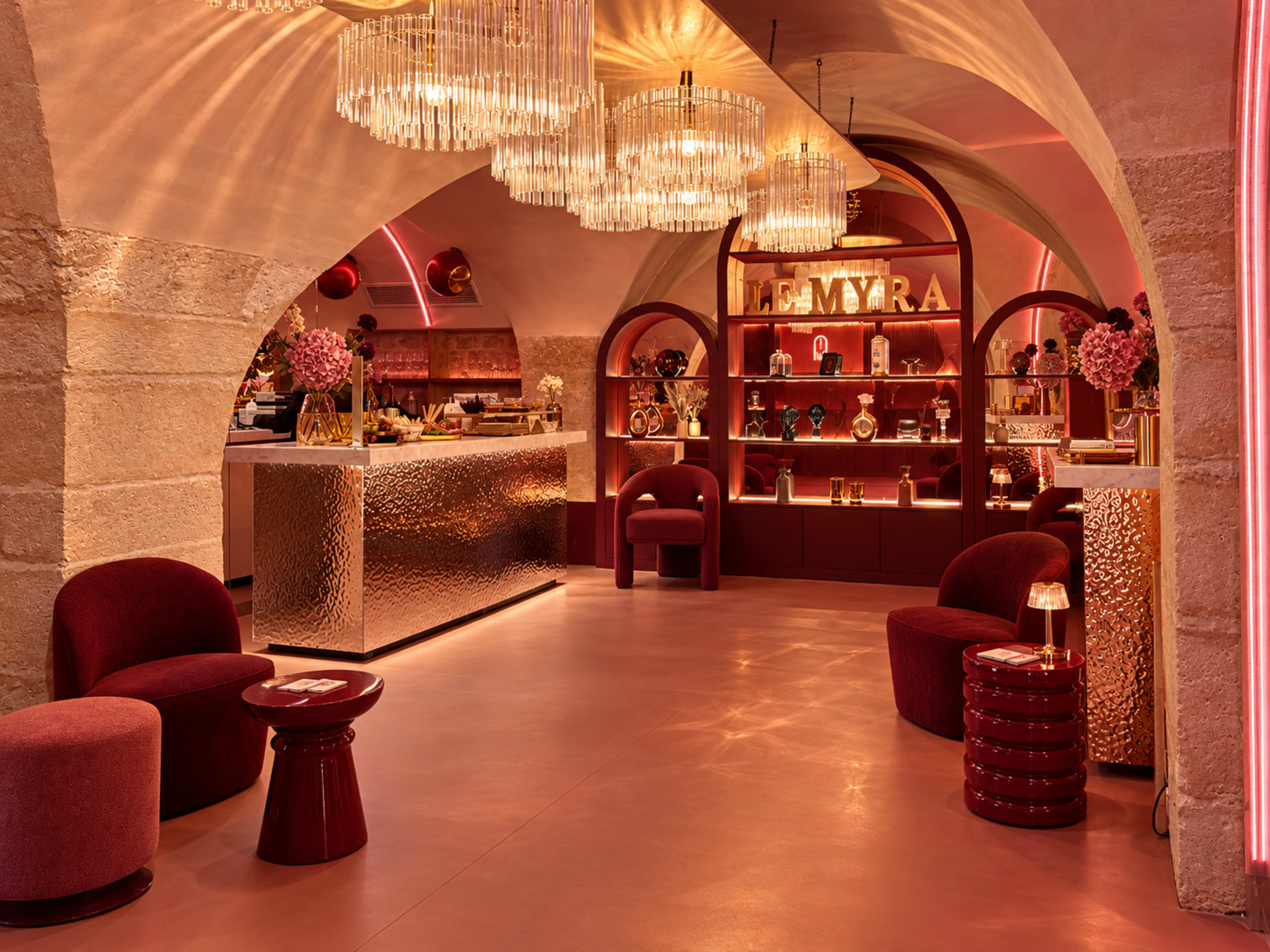 The image shows a stylish underground bar with modern decor, featuring plush seating, decorative lighting, and shelves displaying various bottles and decor items.