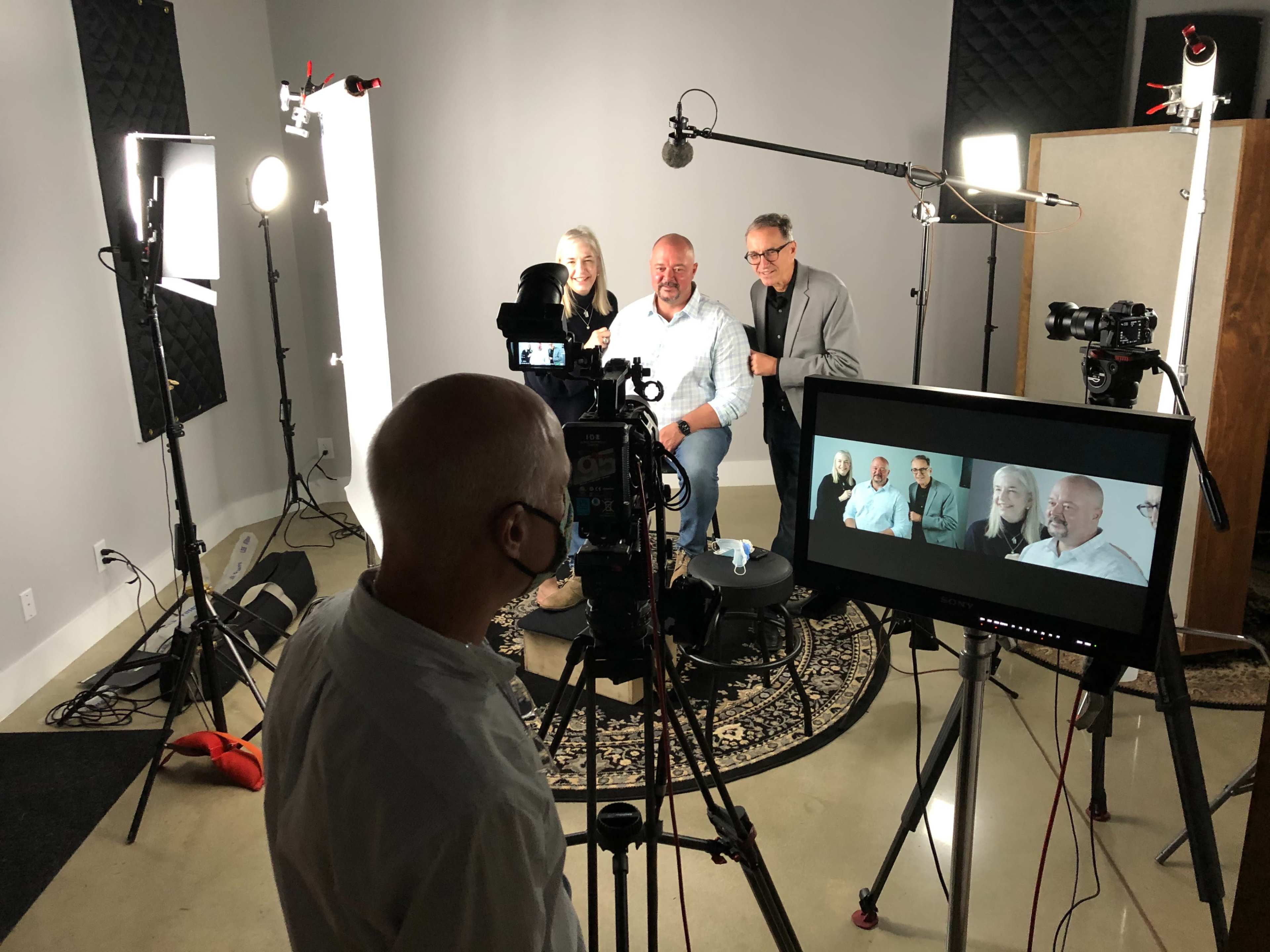 A production team sets up cameras and lighting for an interview featuring two seated individuals in a studio.