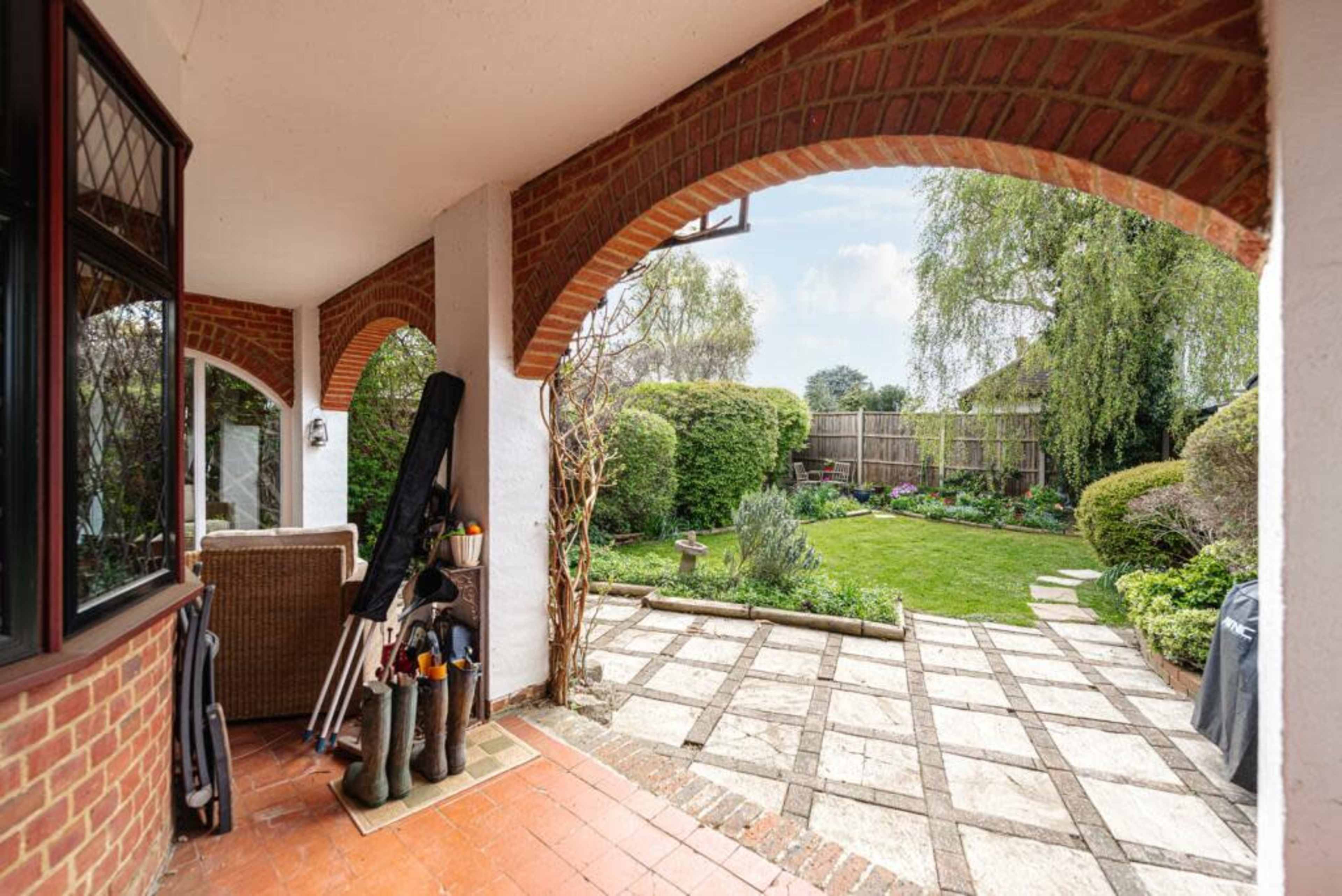 A patio with brick arches overlooking a neatly landscaped garden featuring a stone pathway and various plants.