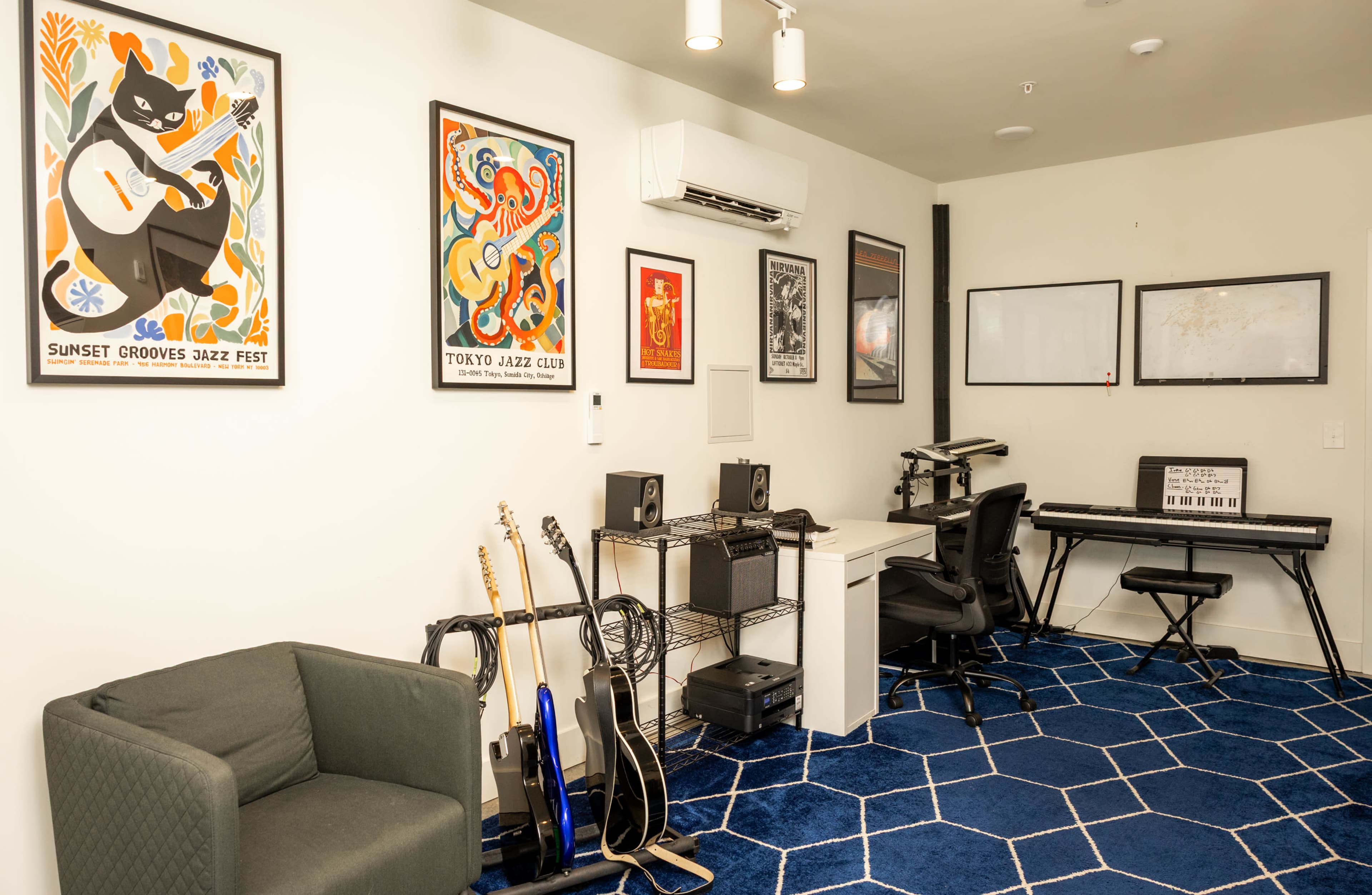 The room features a gray chair, a desk with musical equipment, a keyboard, and framed posters on the walls, with blue geometric patterned flooring.