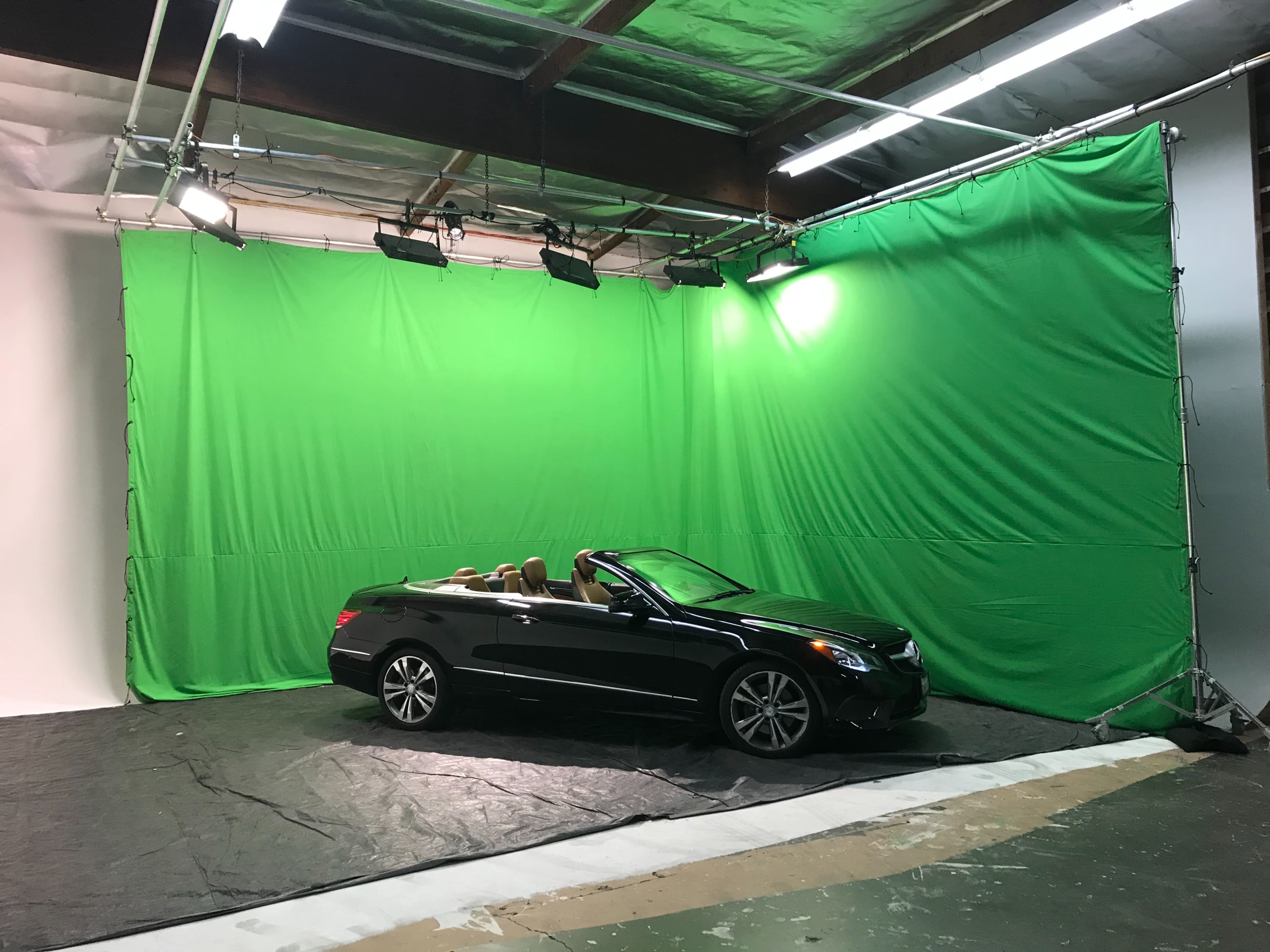 A black convertible car is positioned in front of a green screen in a studio space.