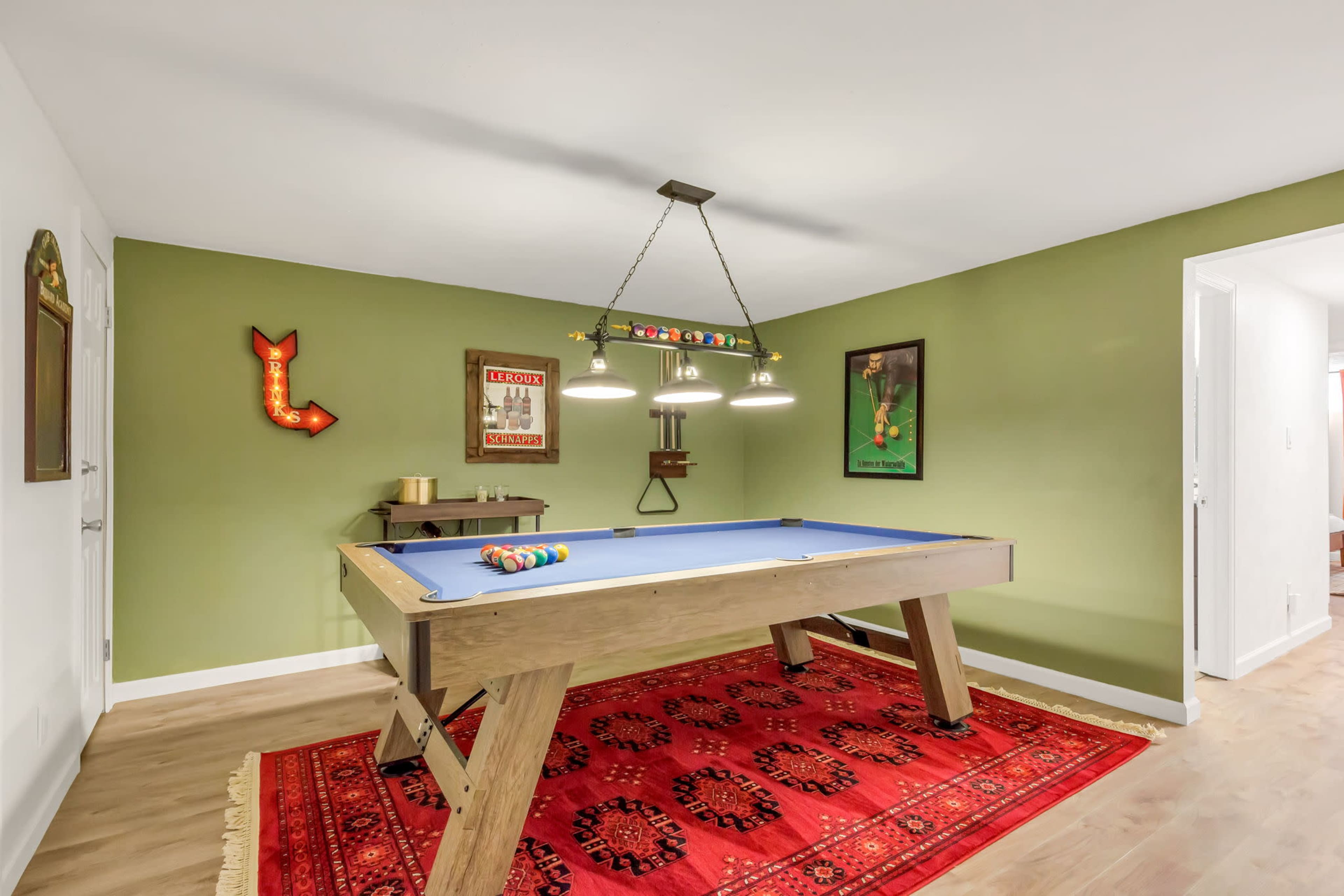 A game room featuring a billiard table with balls arranged on it, a red area rug, and framed artwork on the green walls.