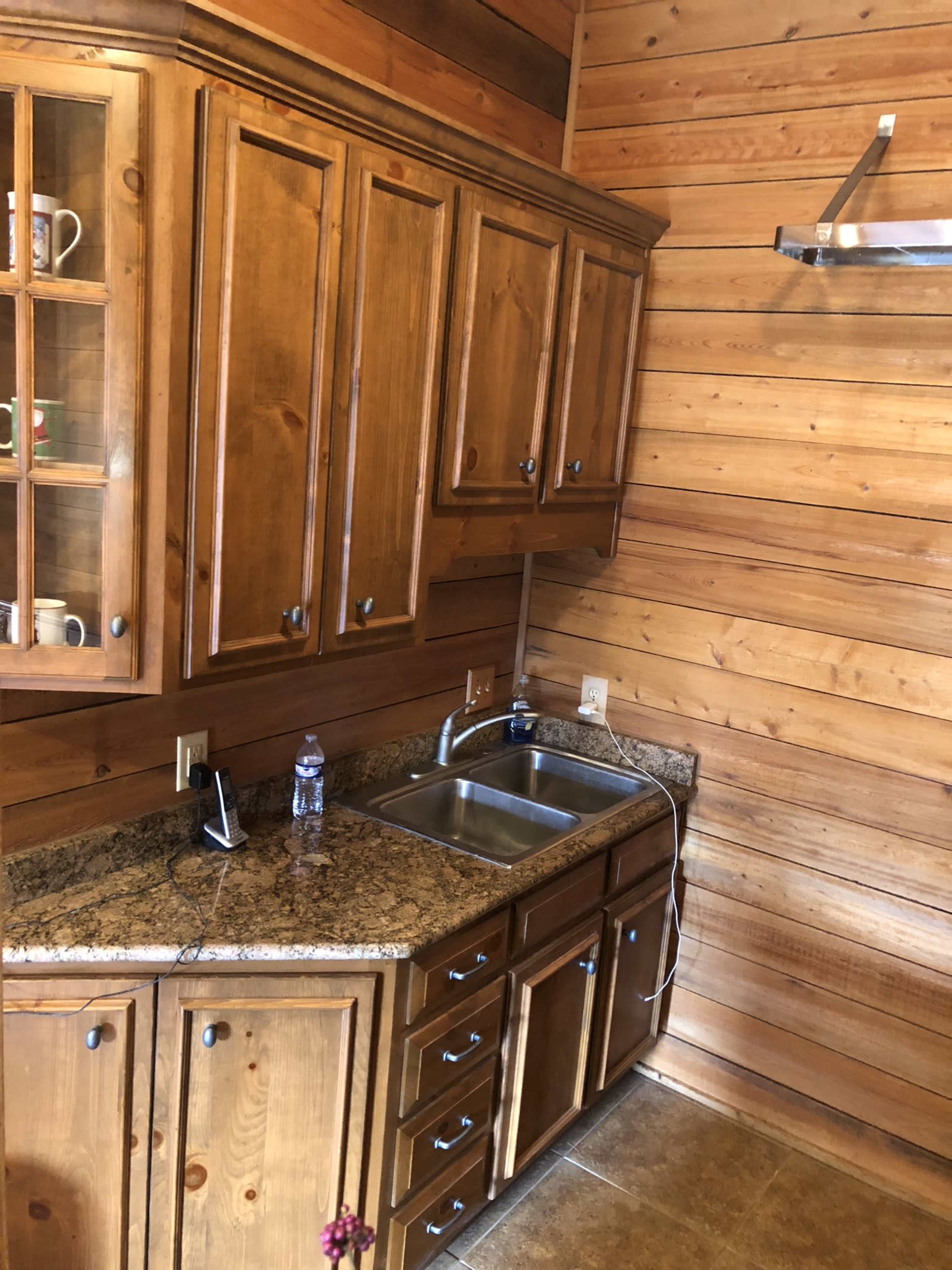 A wooden kitchen area with a stainless steel sink, granite countertops, and wooden cabinets.