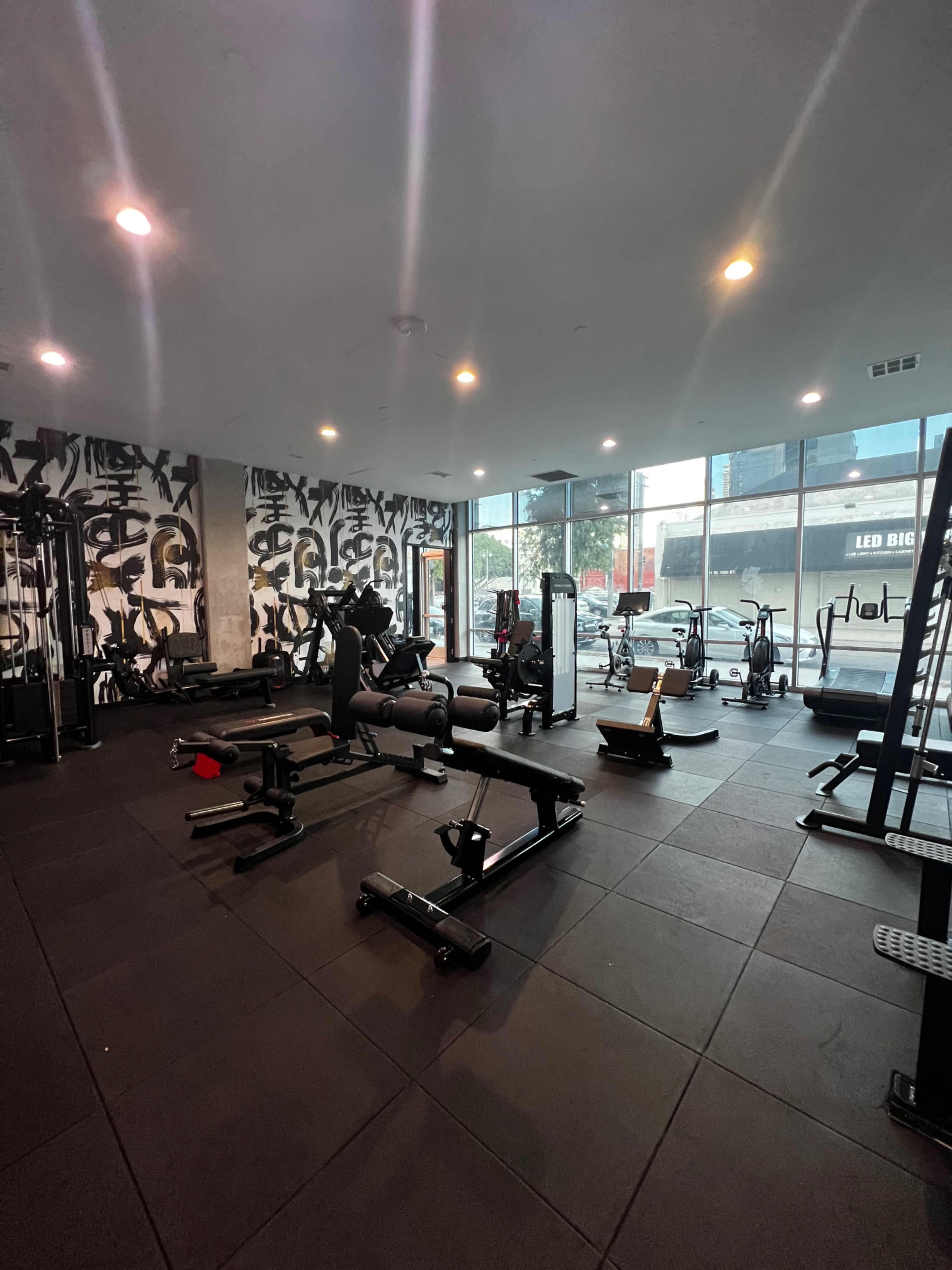 A modern gym interior with various exercise equipment and large windows allowing natural light to enter.