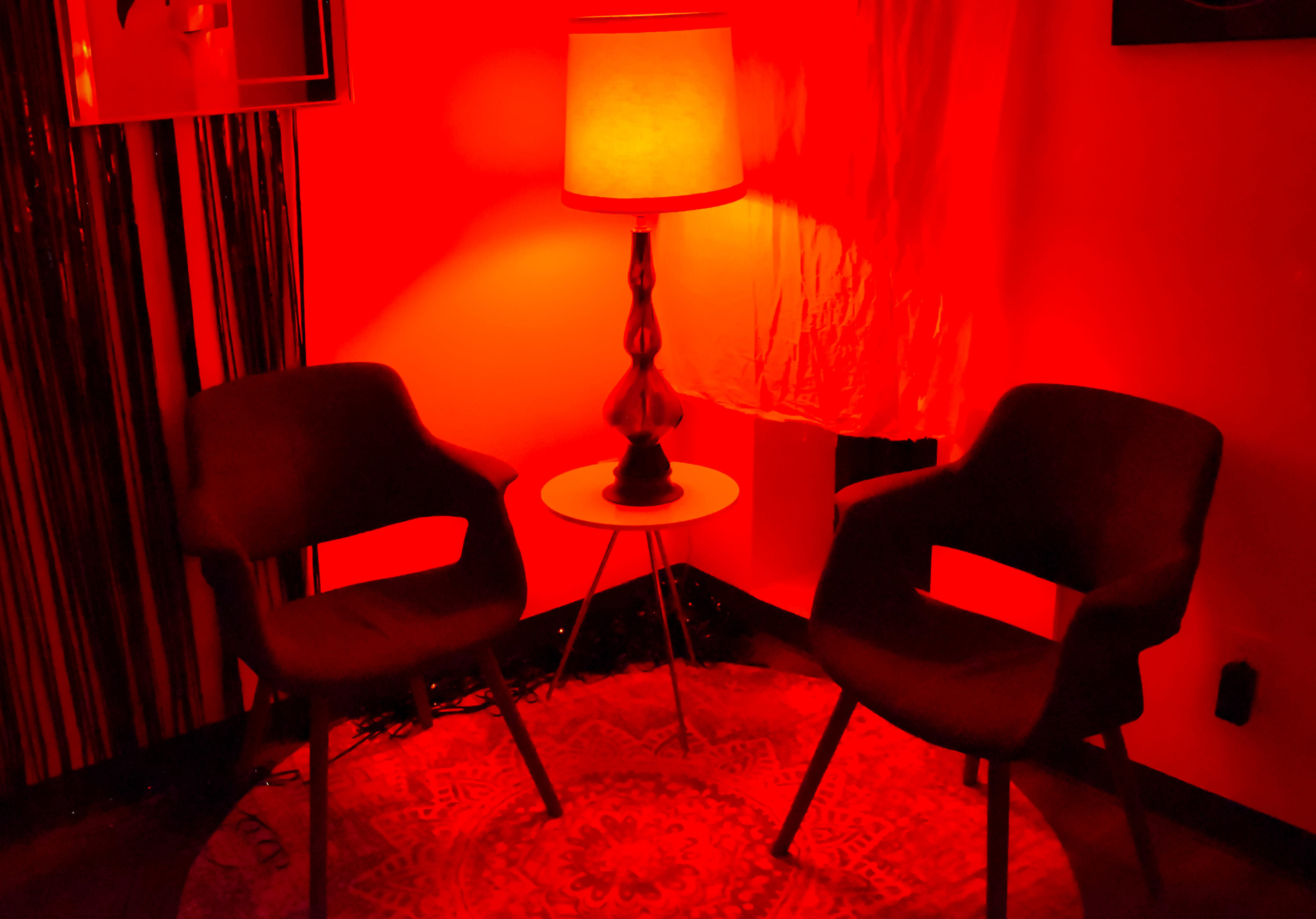The scene features two armchairs positioned near a small table and a lamp, all bathed in red light, with a decorative rug on the floor.