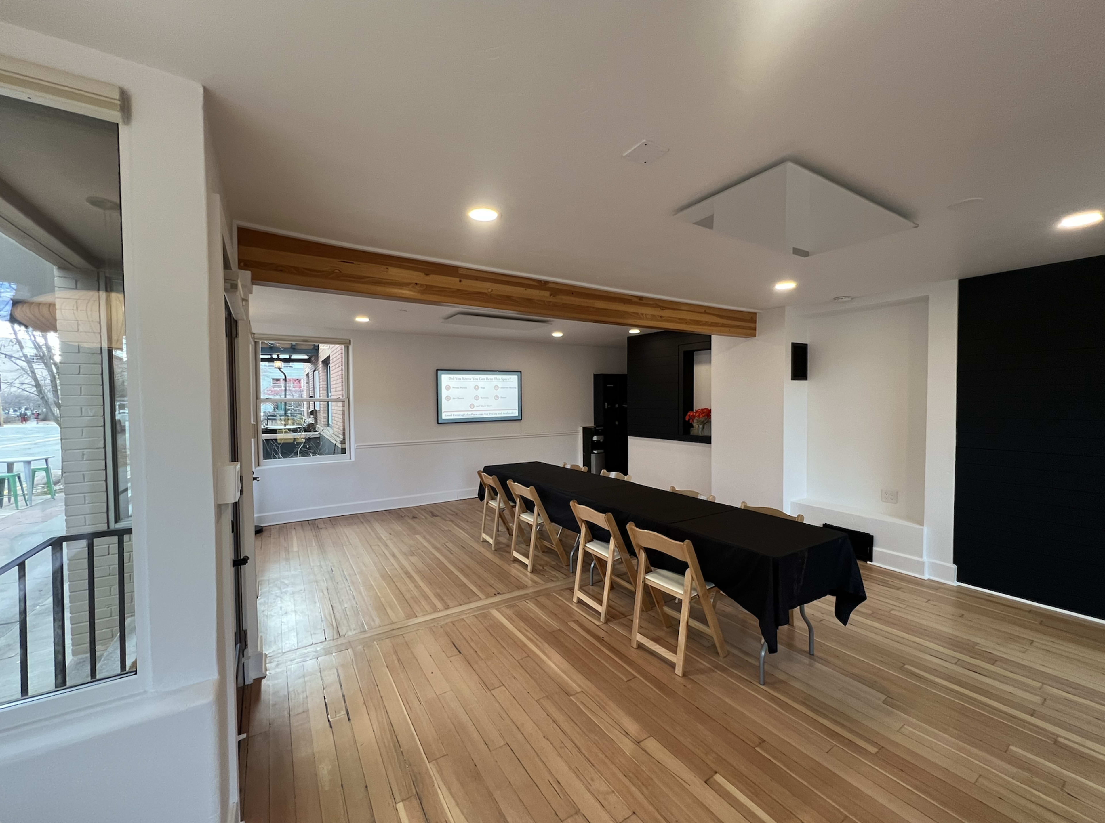 The image shows a conference room with a long table set for a meeting, black tablecloth, and a screen on the wall displaying a presentation.