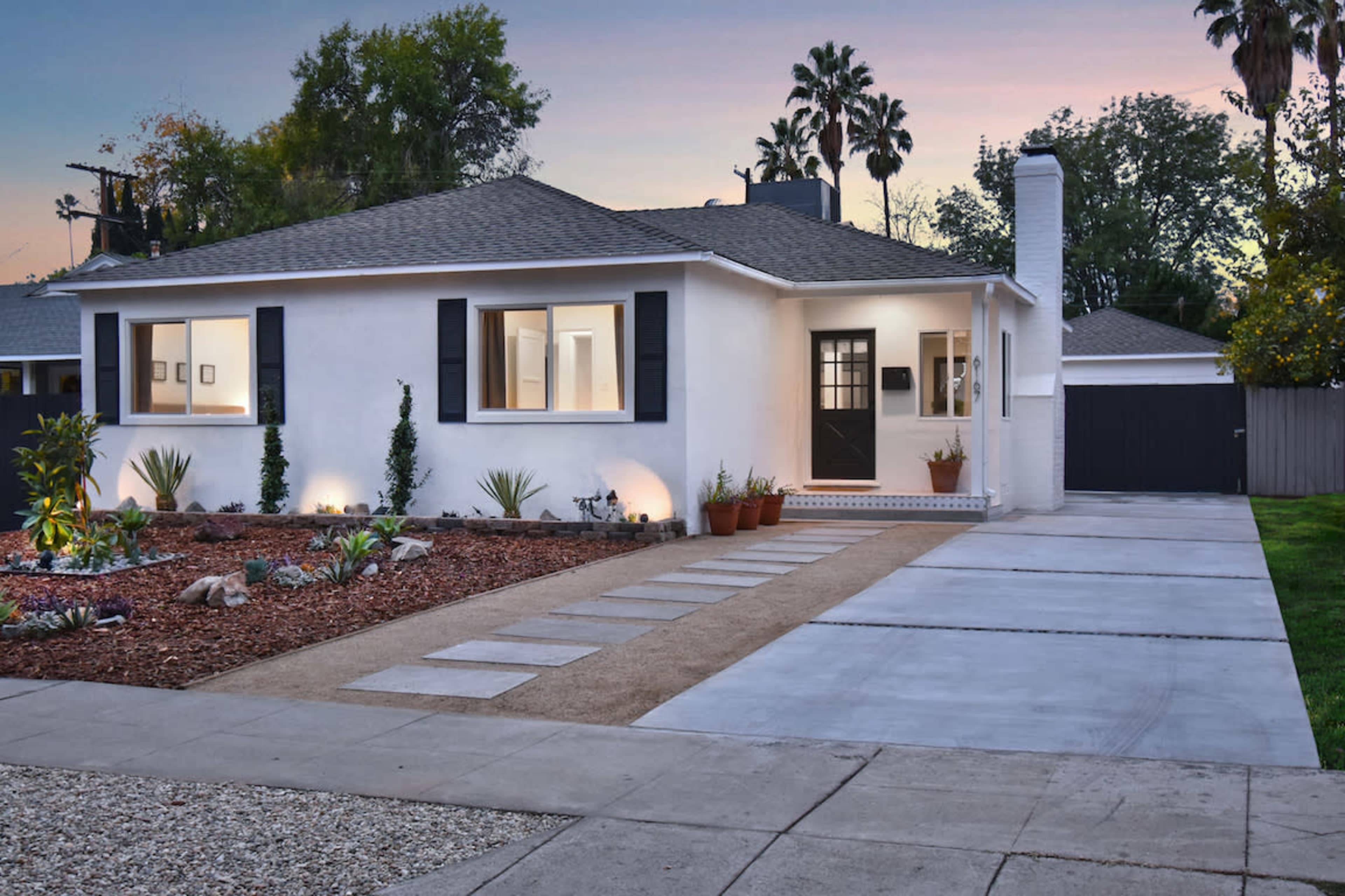 The image shows a modern house with a well-maintained front yard, featuring a mix of gravel and concrete pathways leading up to the entrance.