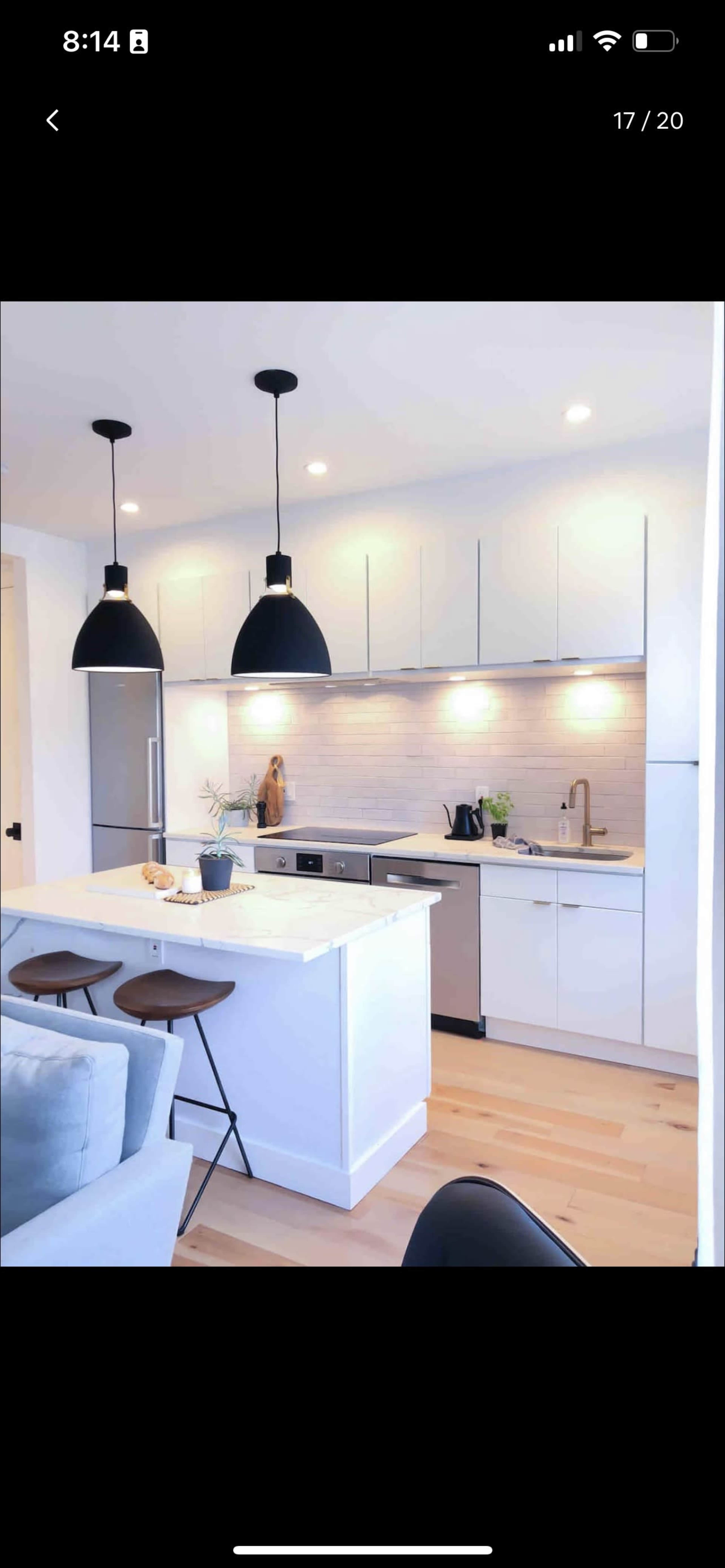 A modern kitchen features sleek white cabinetry, stainless steel appliances, and pendant lighting above a central island with seating.