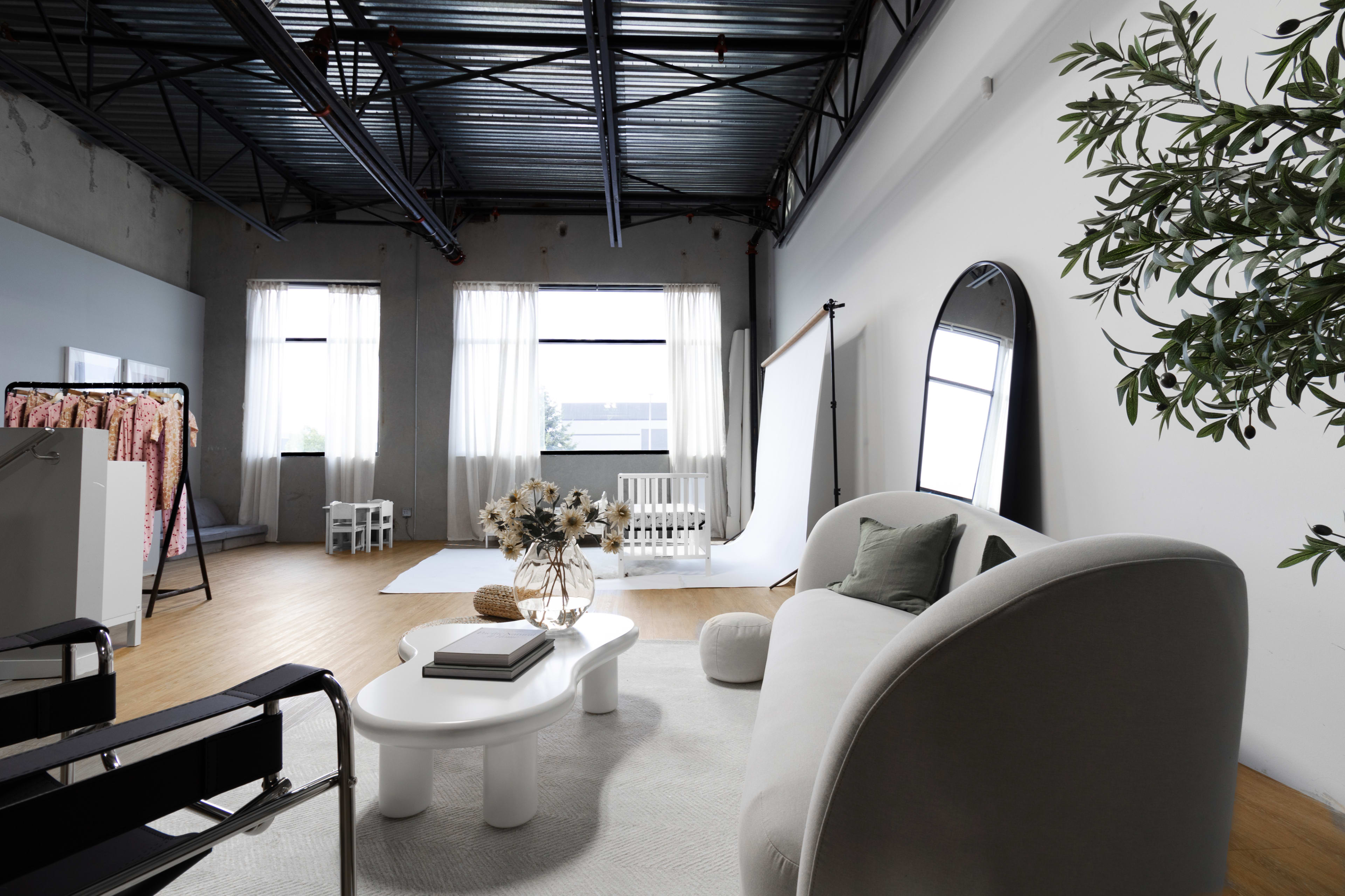 A modern indoor space featuring a light-colored sofa, a coffee table, large windows with sheer curtains, and a backdrop for photography.