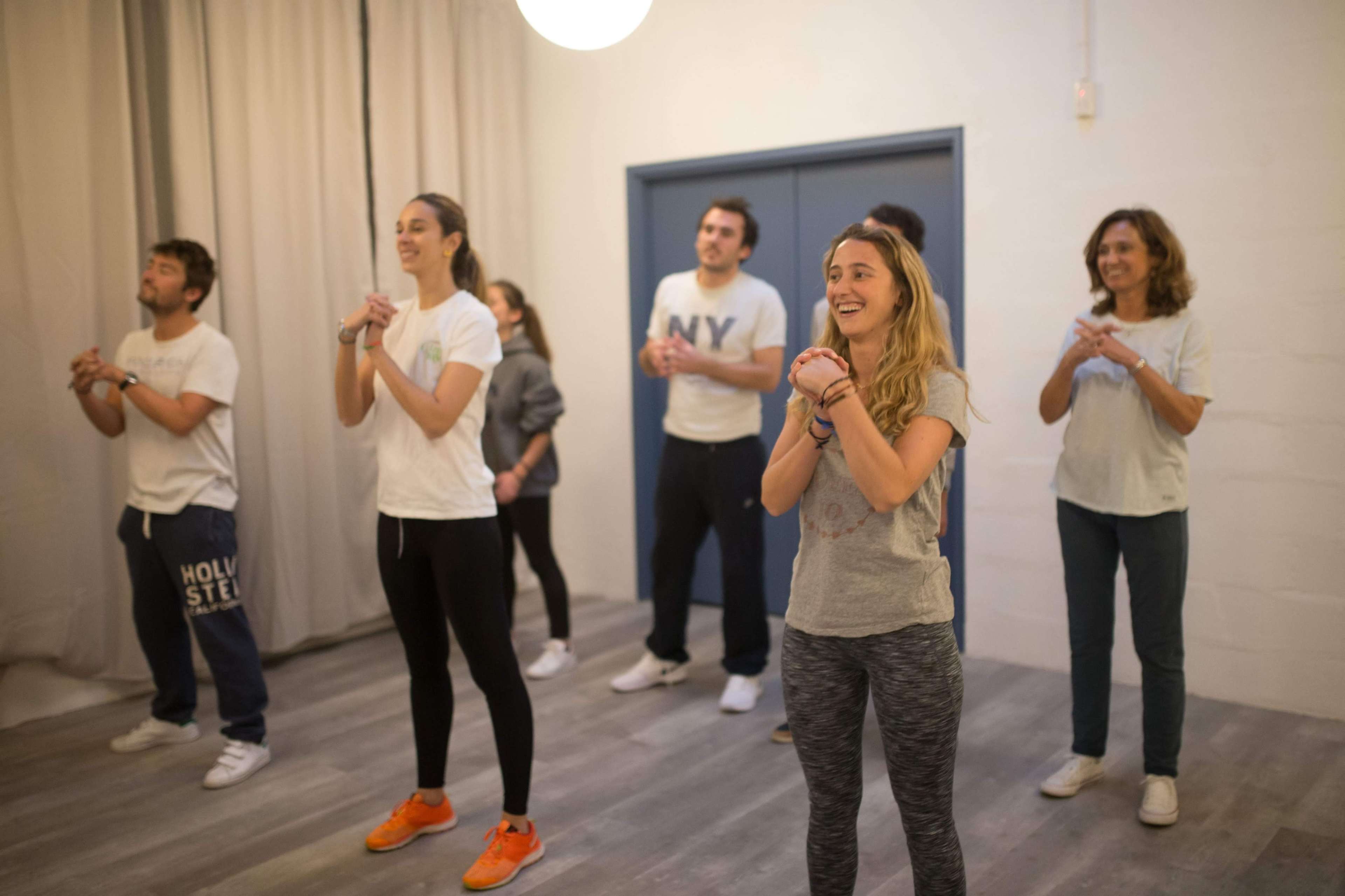 A group of seven people are participating in a movement or exercise class in a brightly lit room.