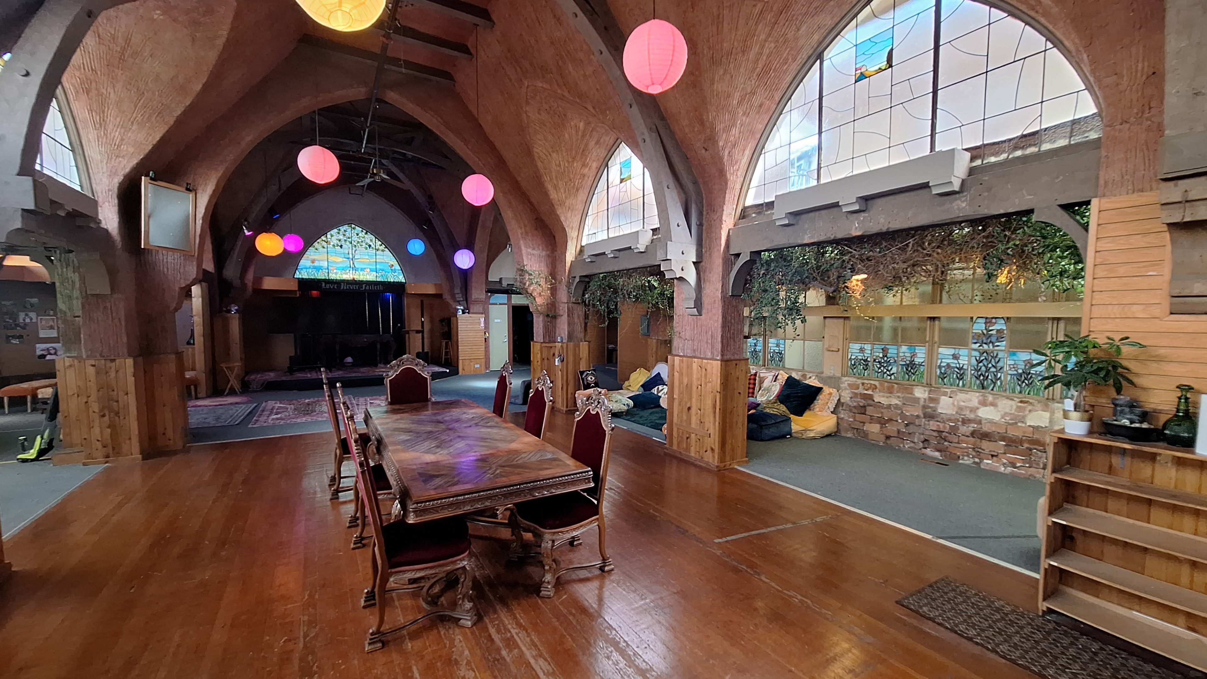 The image shows a spacious room with arched ceilings, a long wooden table surrounded by chairs, and colorful decorative lanterns hanging from the ceiling.