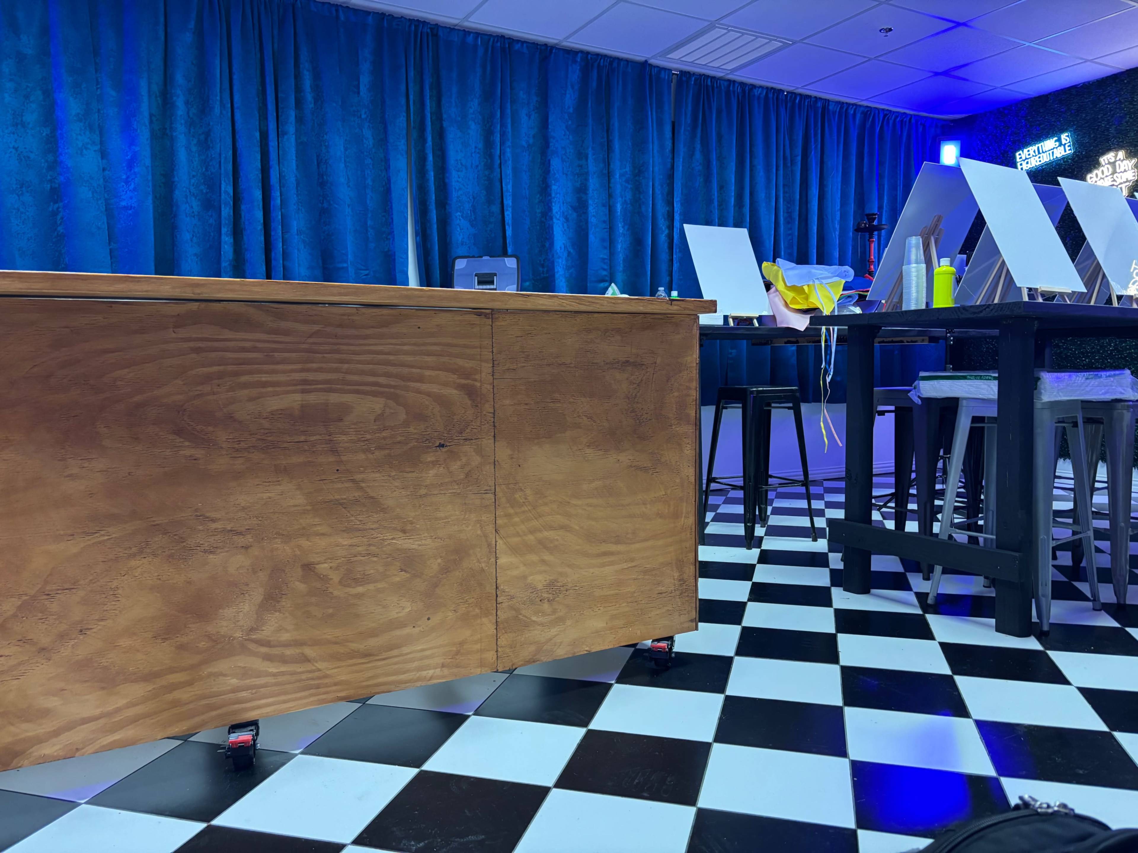 The image shows a room with a checkered black and white floor, a wooden table in the foreground, and blue curtains on the walls.
