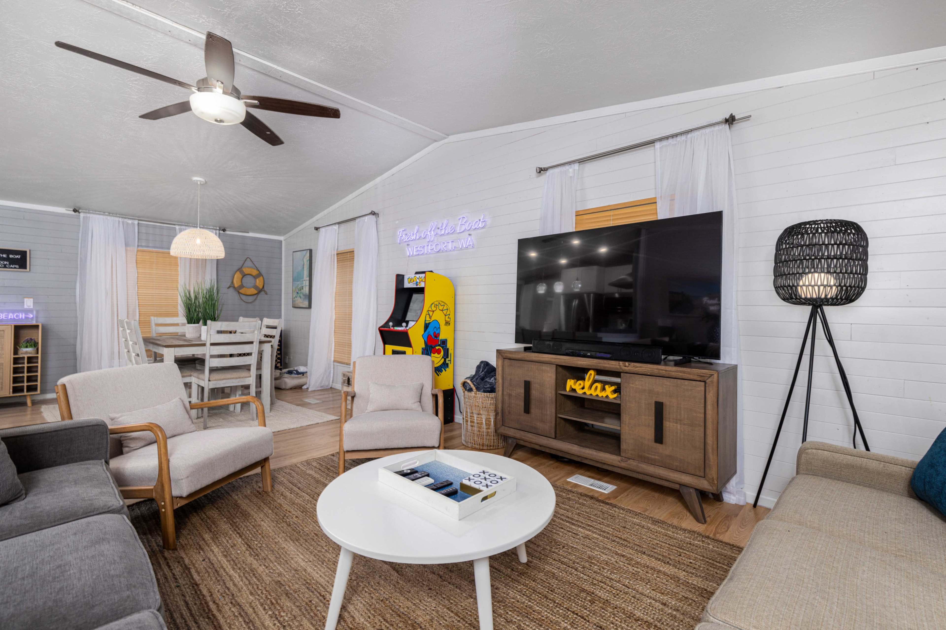 The living room features a television cabinet, a round coffee table, seating arrangements, and an arcade machine tucked in a corner.
