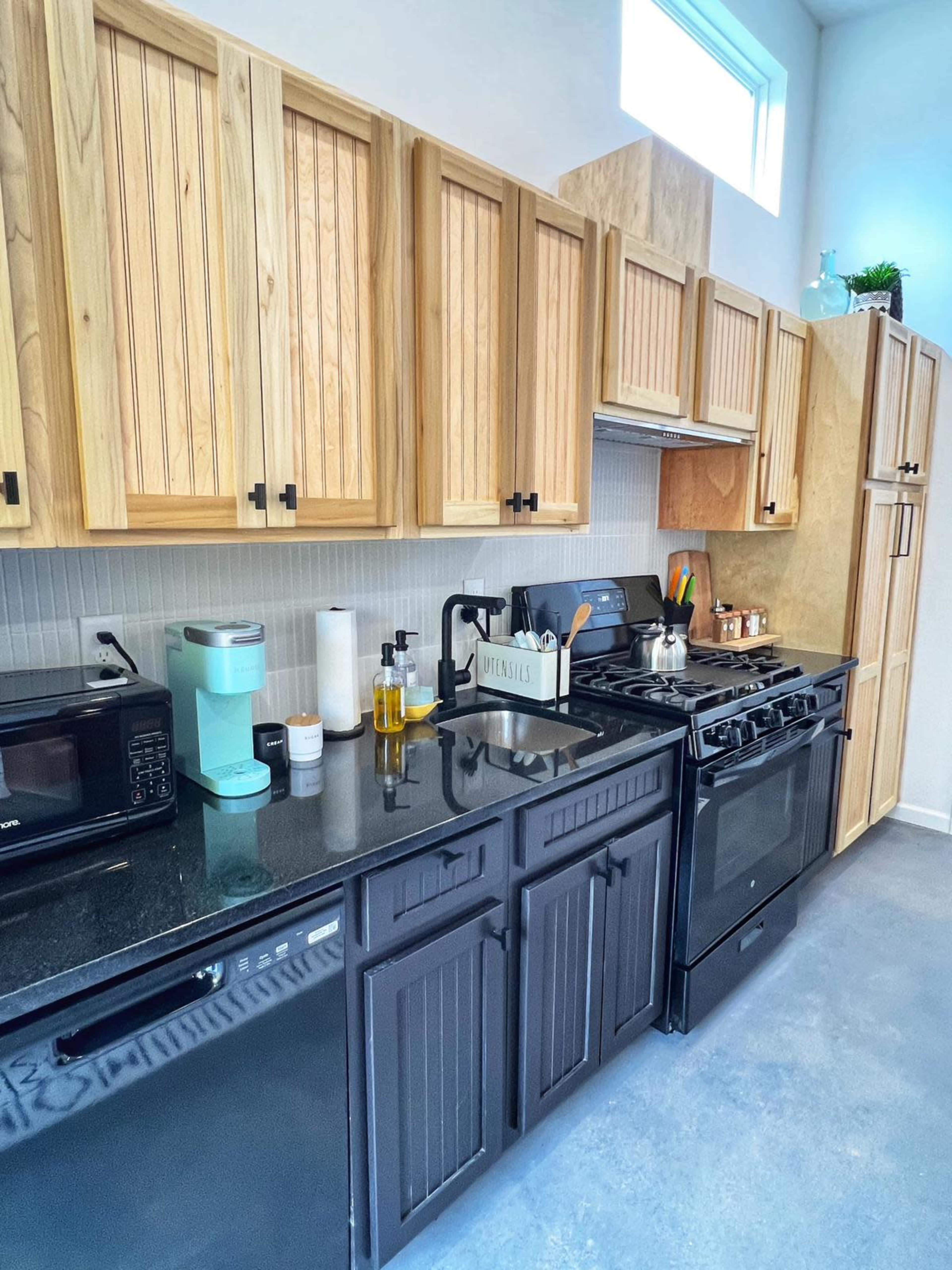 A modern kitchen featuring wooden cabinets, a black refrigerator, a black stove, and a countertop with various cooking utensils and appliances.