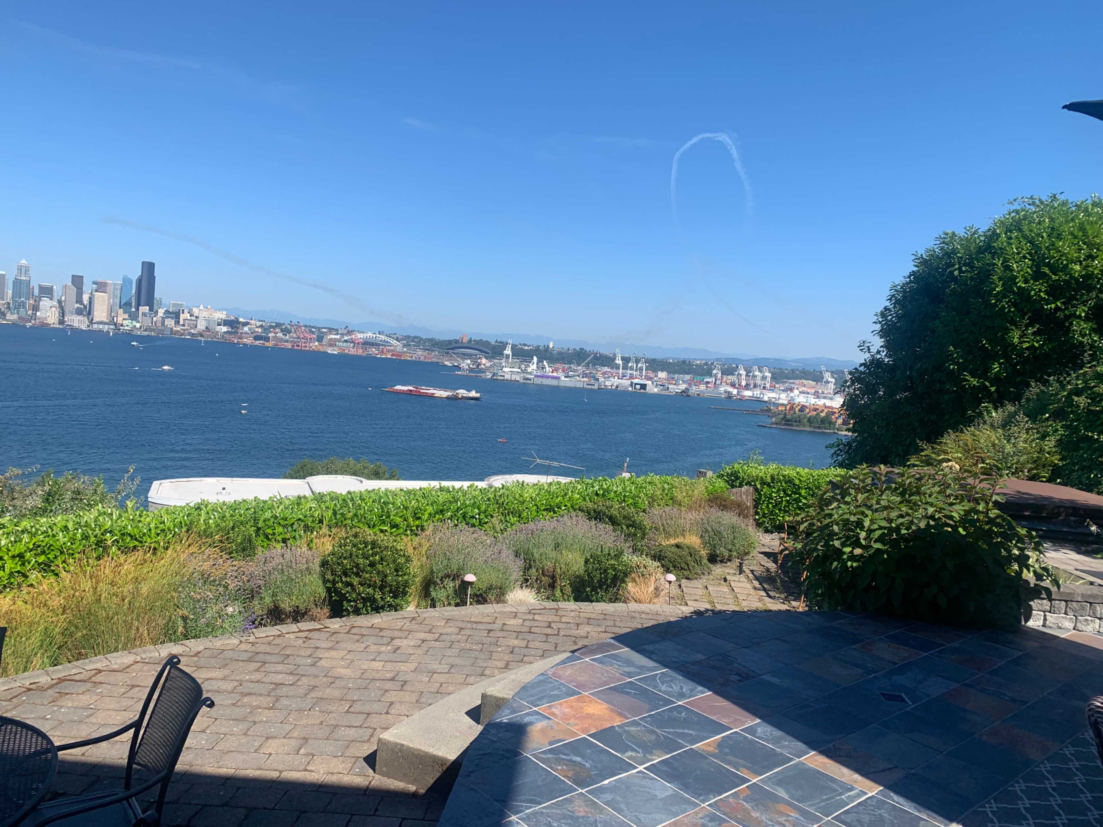 A waterfront view of Seattle featuring the city skyline, boats on the water, and green landscaping in the foreground.