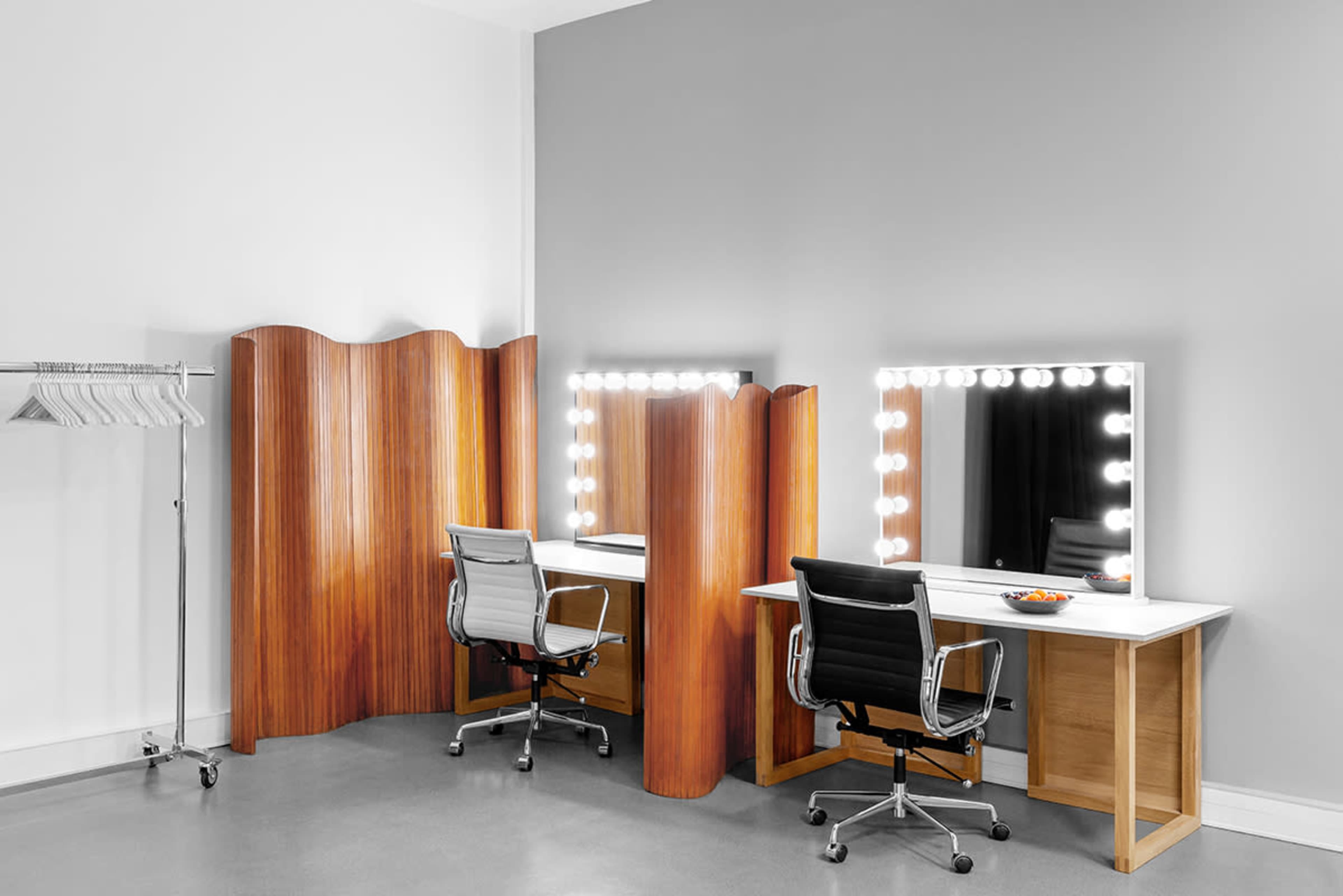 A minimalist dressing room with two illuminated mirrors flanked by wooden dividers and a clothing rack in the corner.