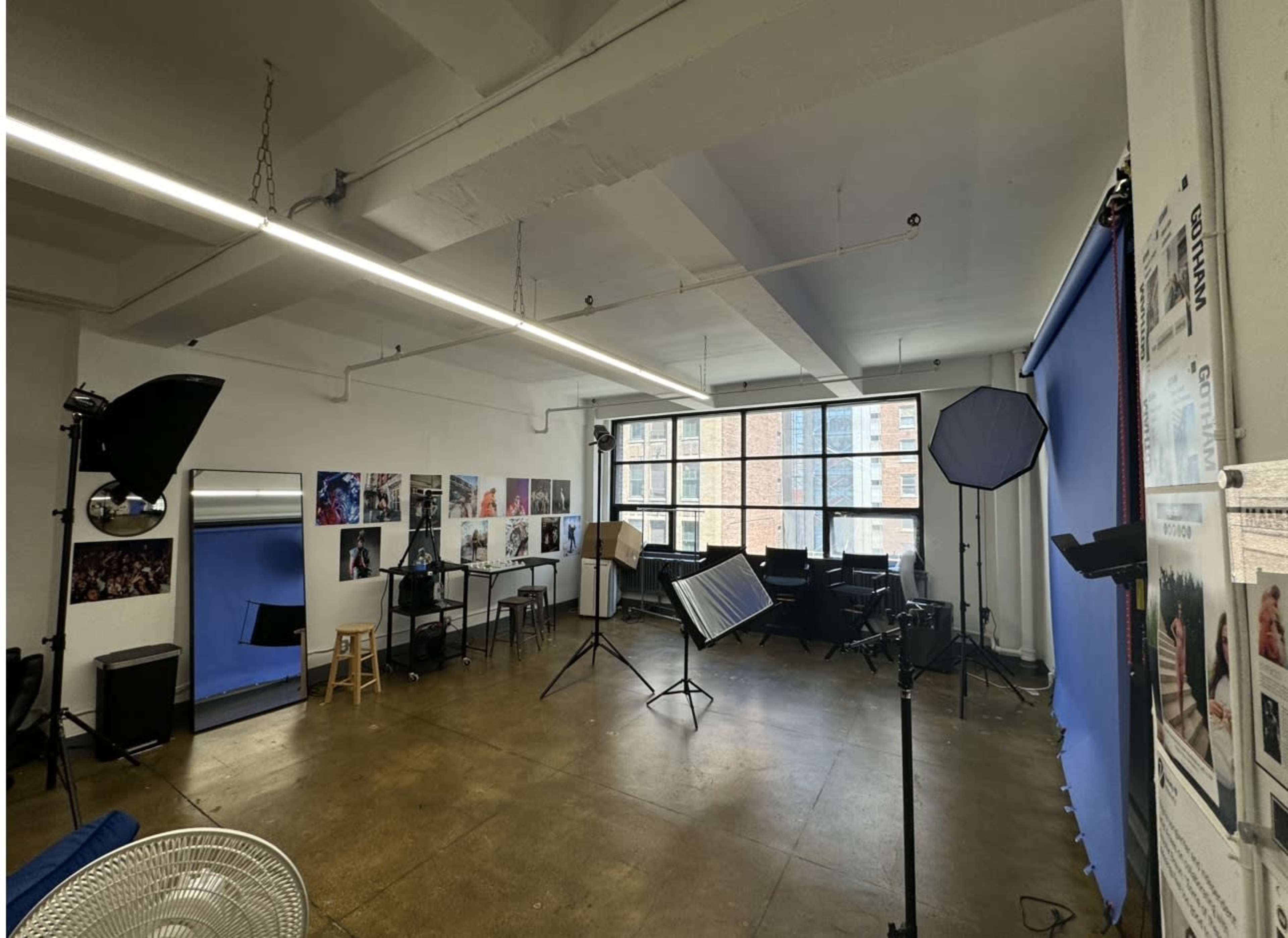 A photography studio with a blue backdrop, various lighting equipment, and several photo displays on the walls.