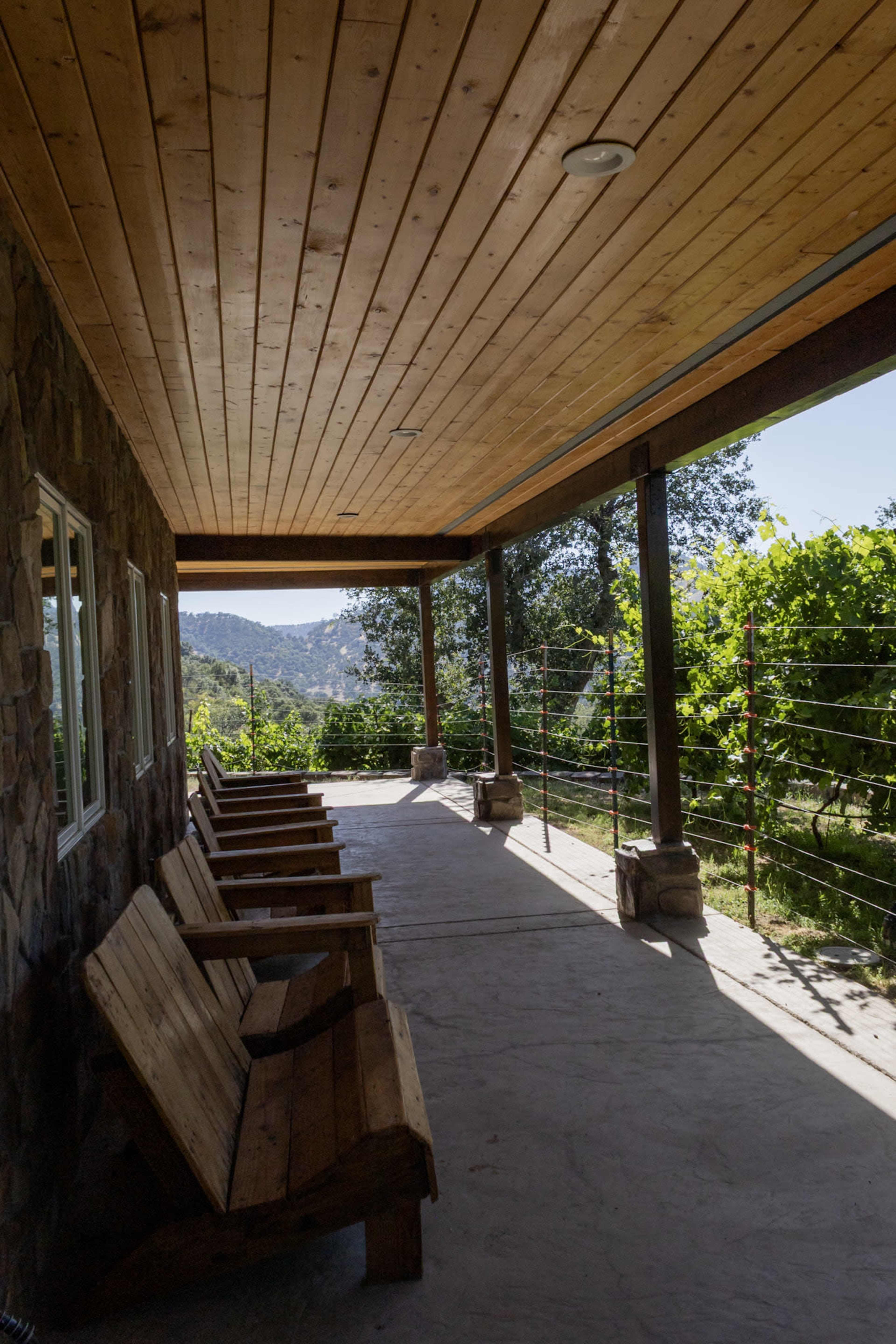 A covered porch with wooden benches overlooks a vineyard and rolling hills.