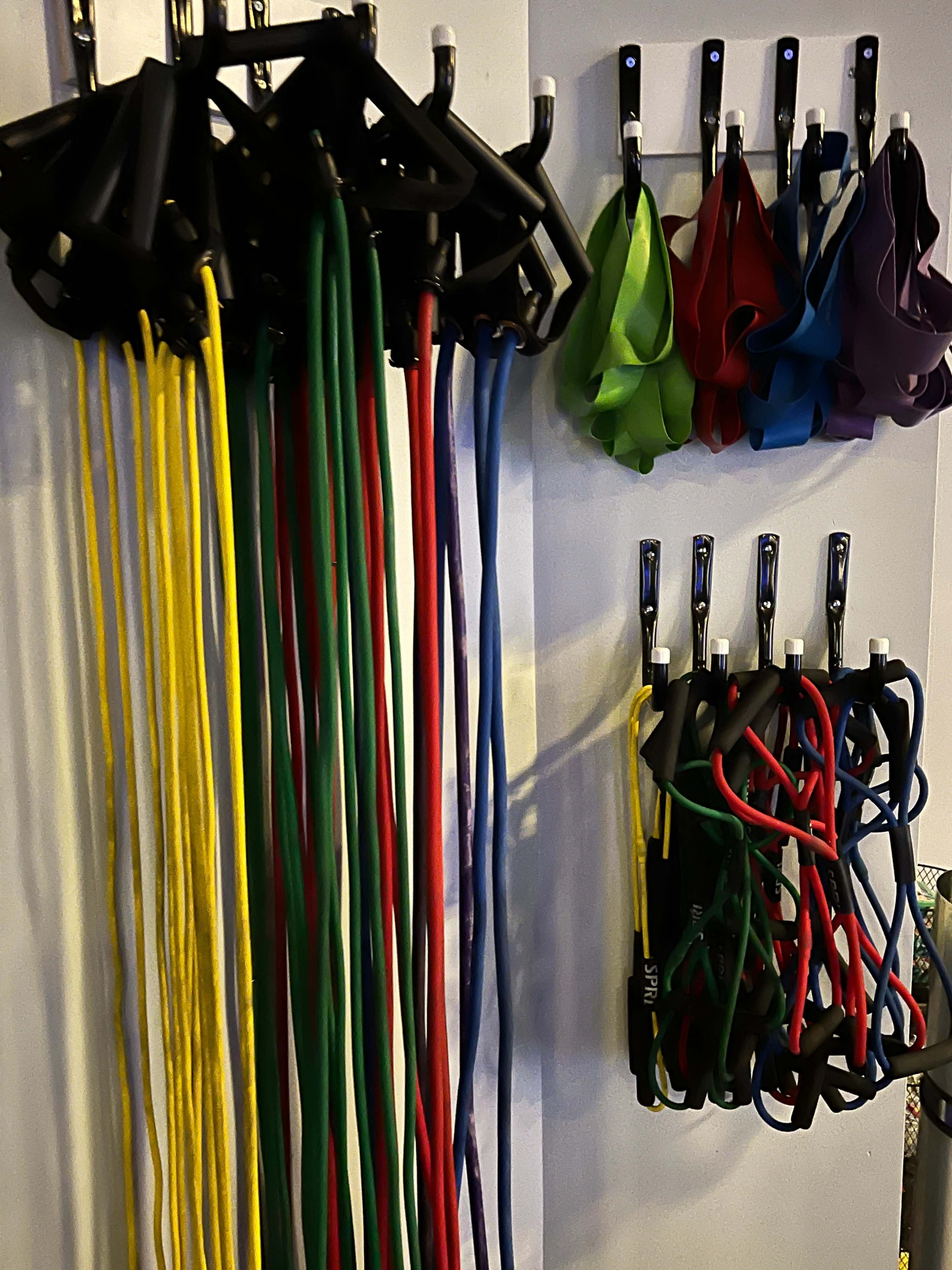 A wall-mounted rack with various colored resistance bands and exercise equipment neatly organized on hooks.