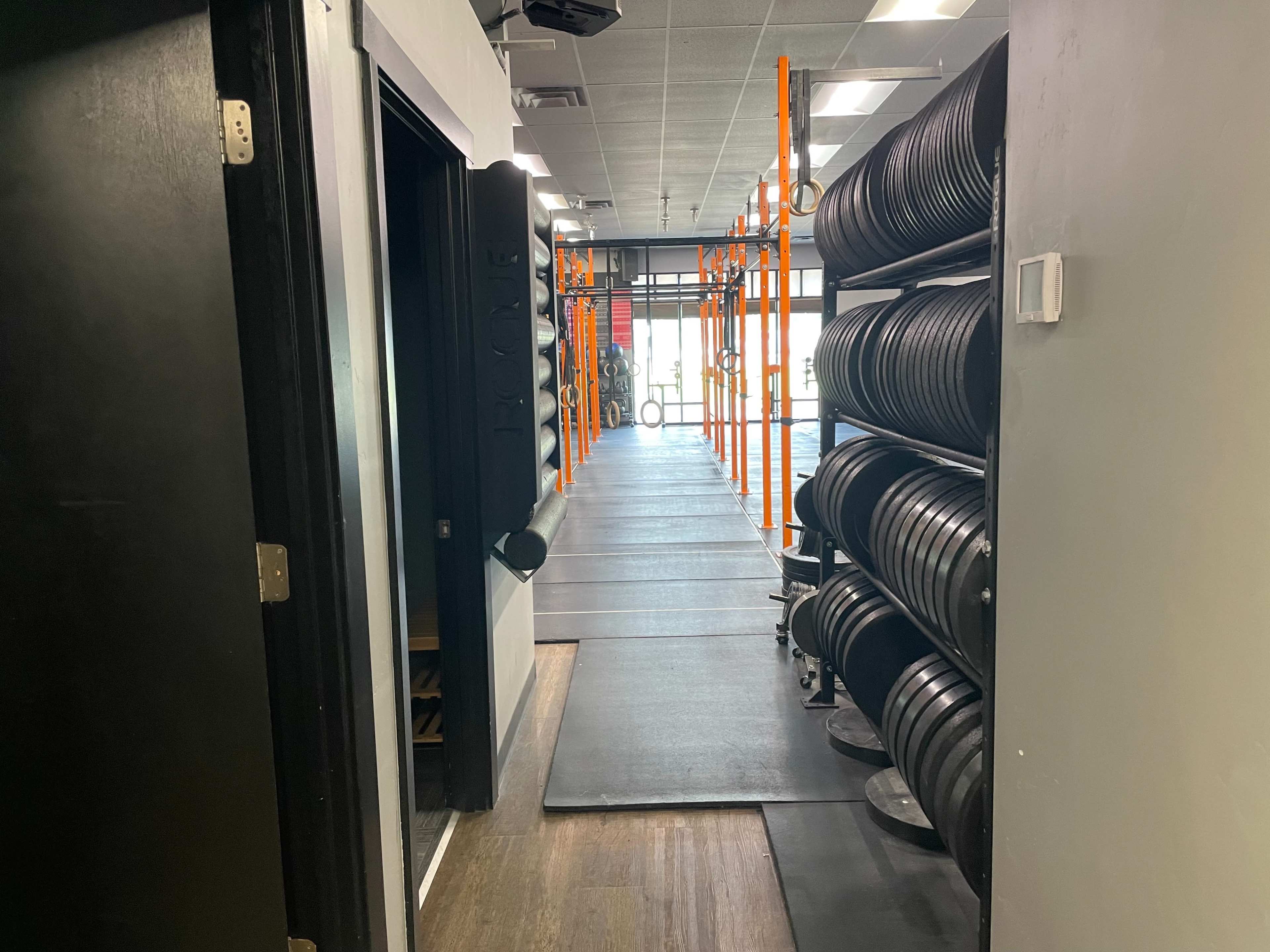 A gym corridor lined with weightlifting plates on racks and a pathway leading to an entrance.