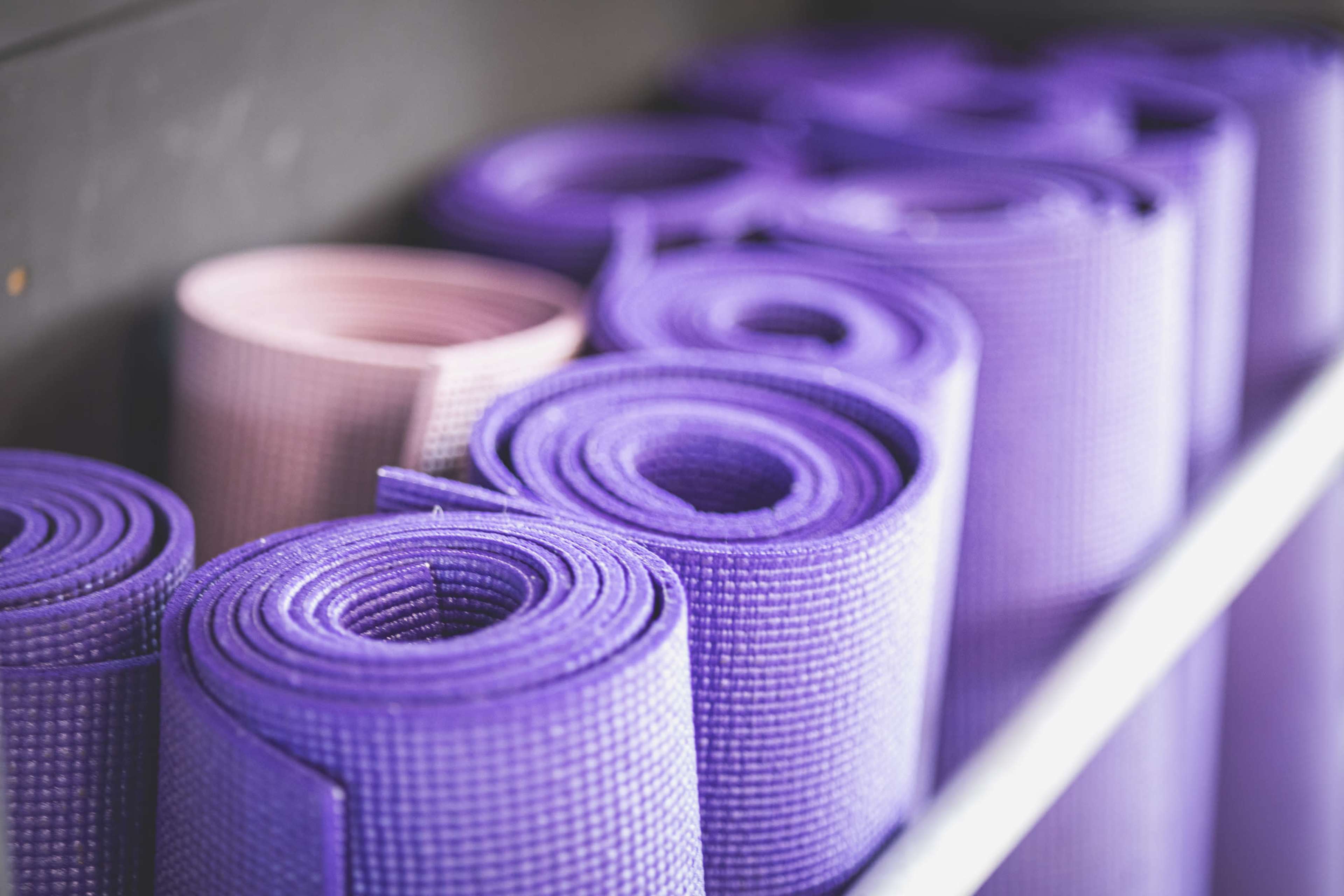 Stacked yoga mats in shades of purple and pink are neatly arranged on a shelf.