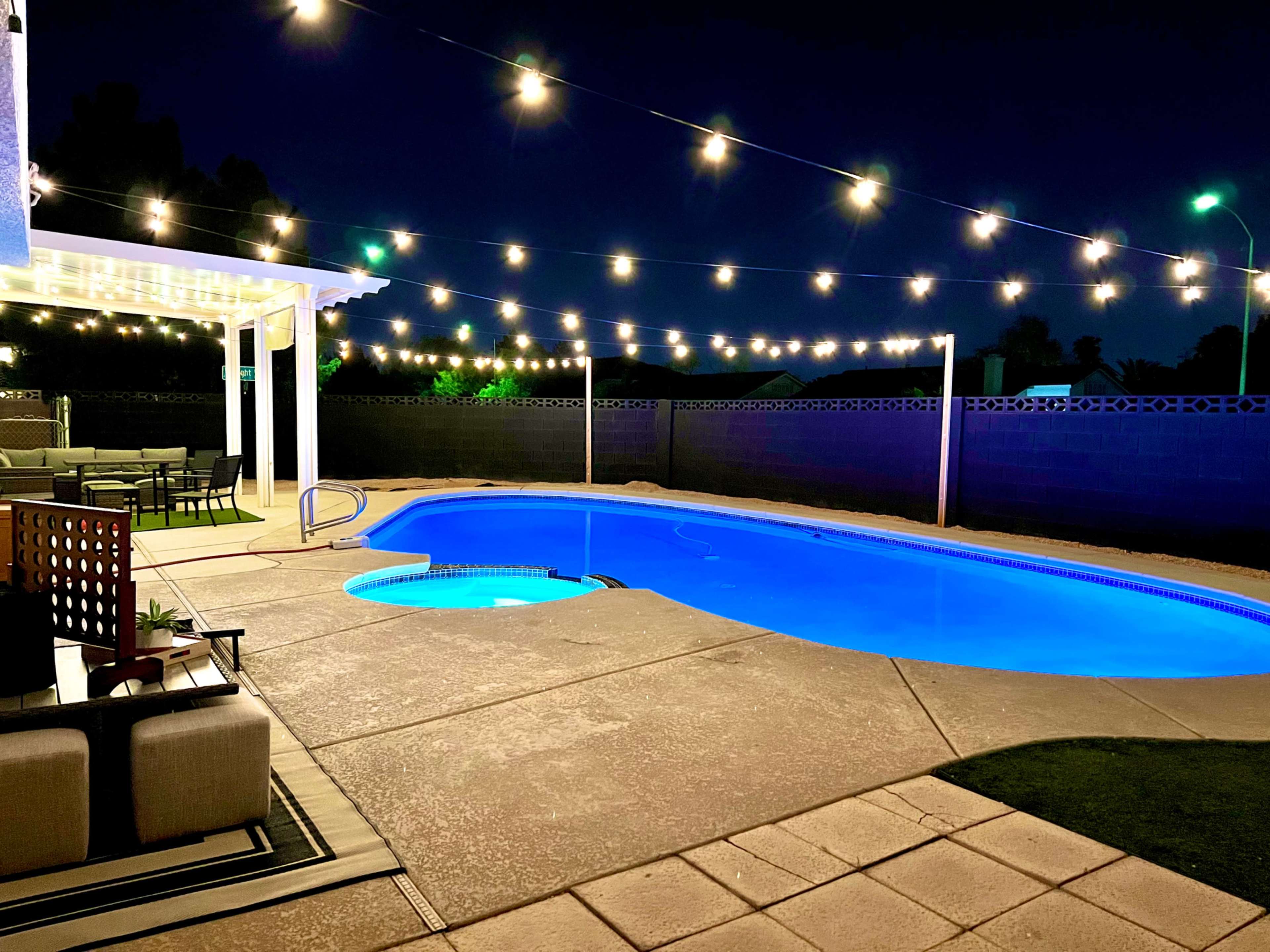 The scene features a backyard with a swimming pool illuminated by blue lights, surrounded by string lights and patio furniture.