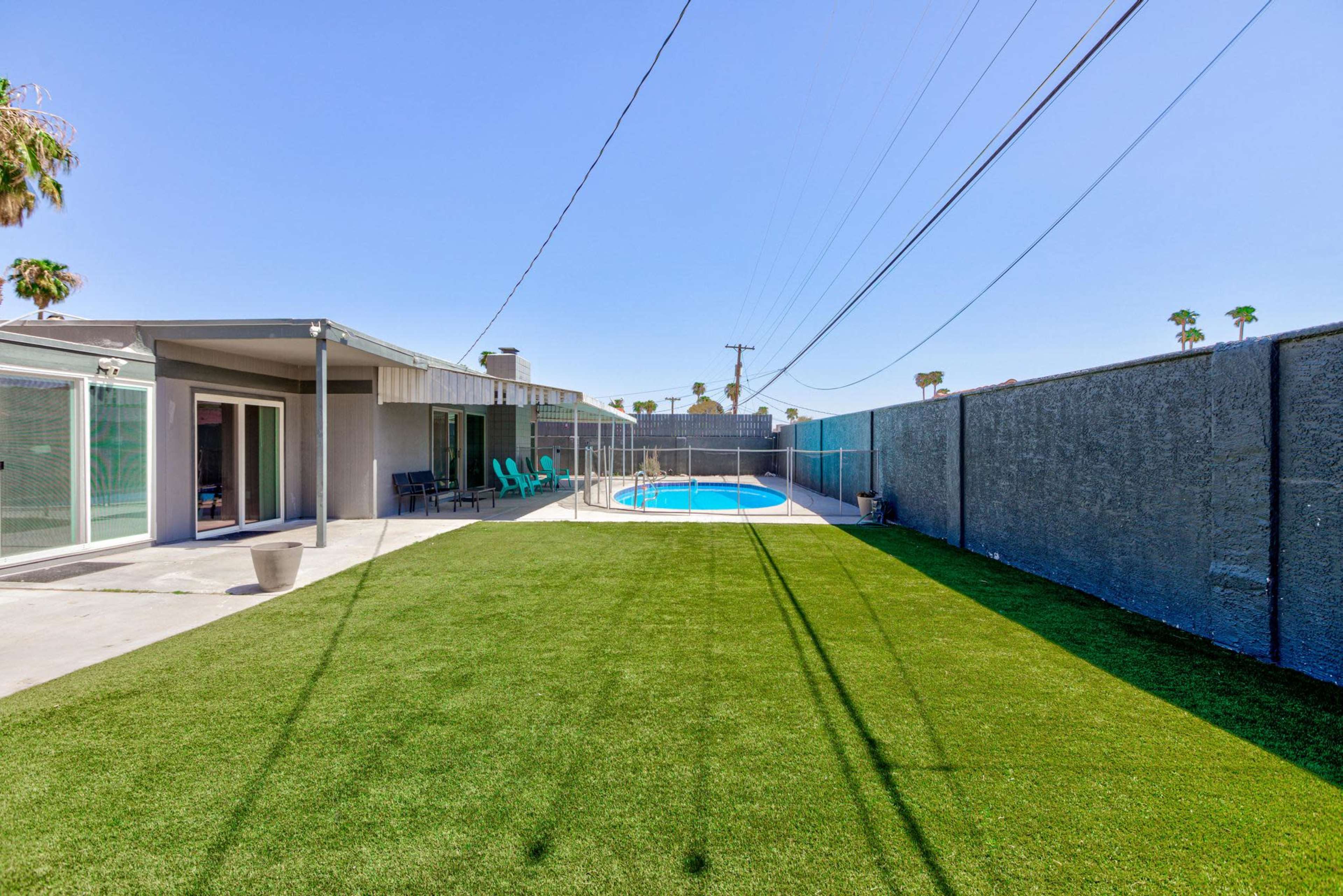 The image shows a backyard with synthetic grass, a swimming pool, and a modern house with sliding glass doors.