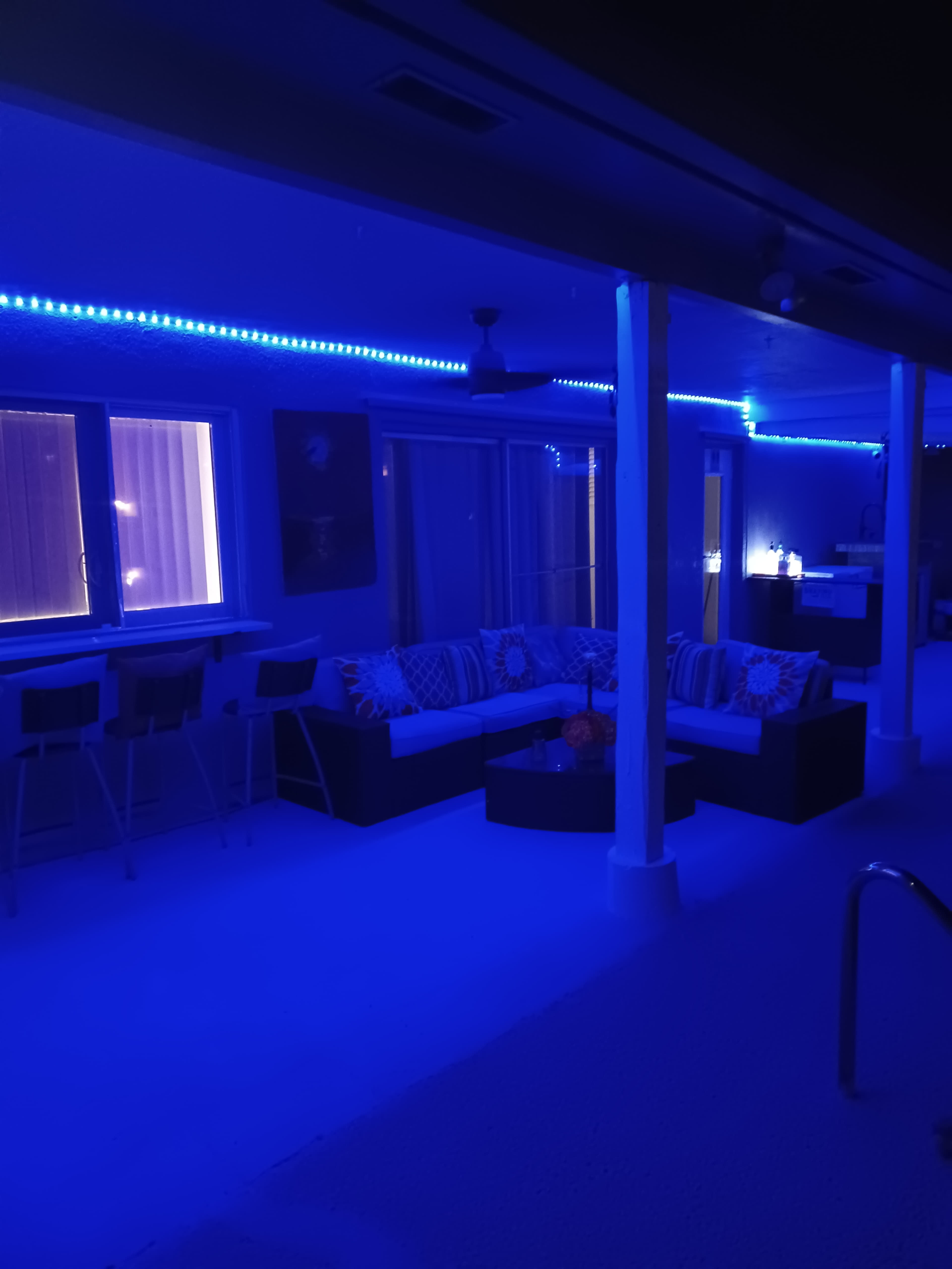 A patio area features a sectional sofa, bar stools, and is illuminated by blue LED lights.