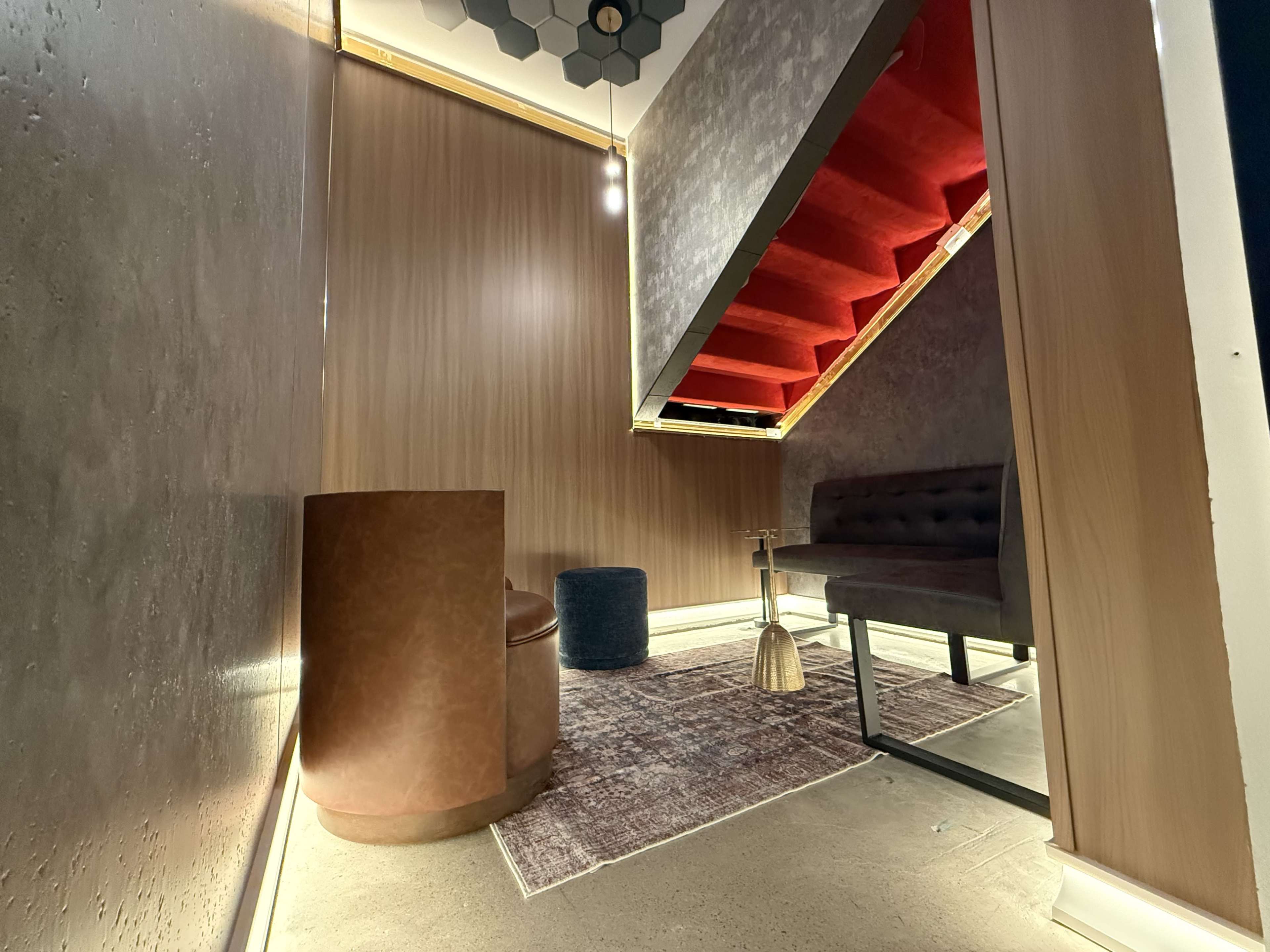 The image shows a stylized interior space featuring a staircase with red steps, a small table, a seating area, and warm lighting.