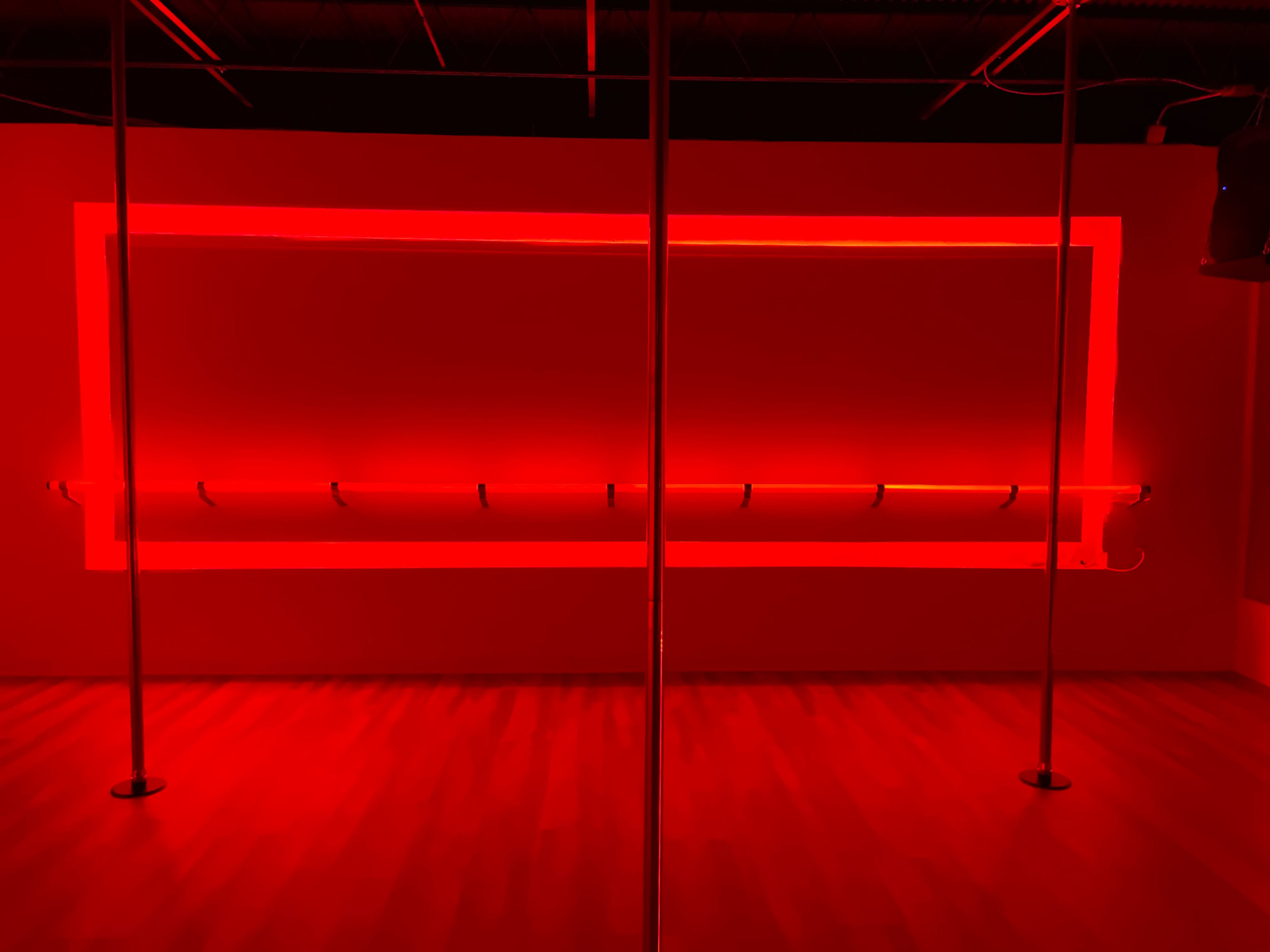 The image features a dimly lit room with red lighting, a polished wooden floor, and a central pole.