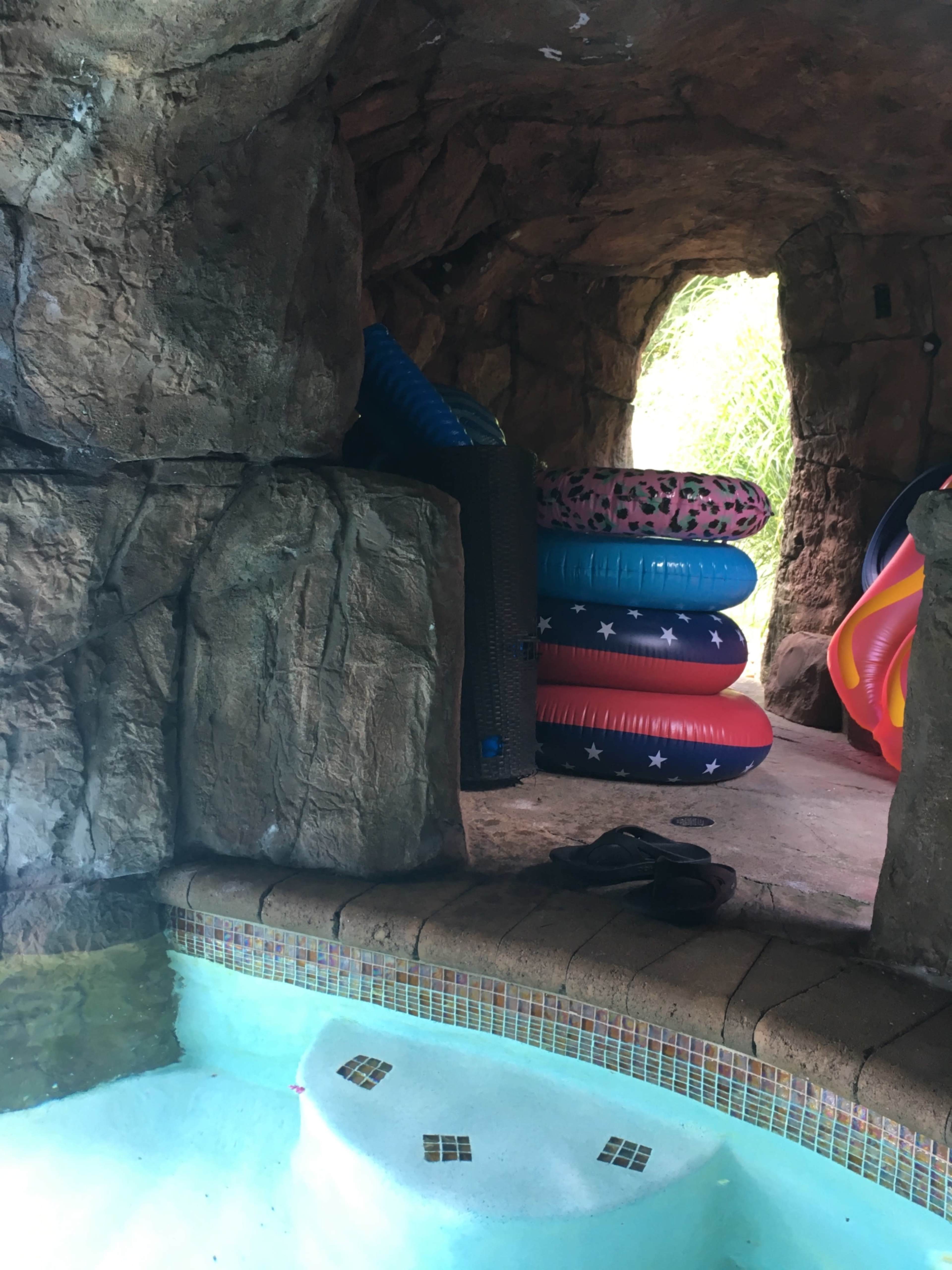 A grotto-like area beside a pool, featuring stacks of colorful inflatable floats against a rocky backdrop.