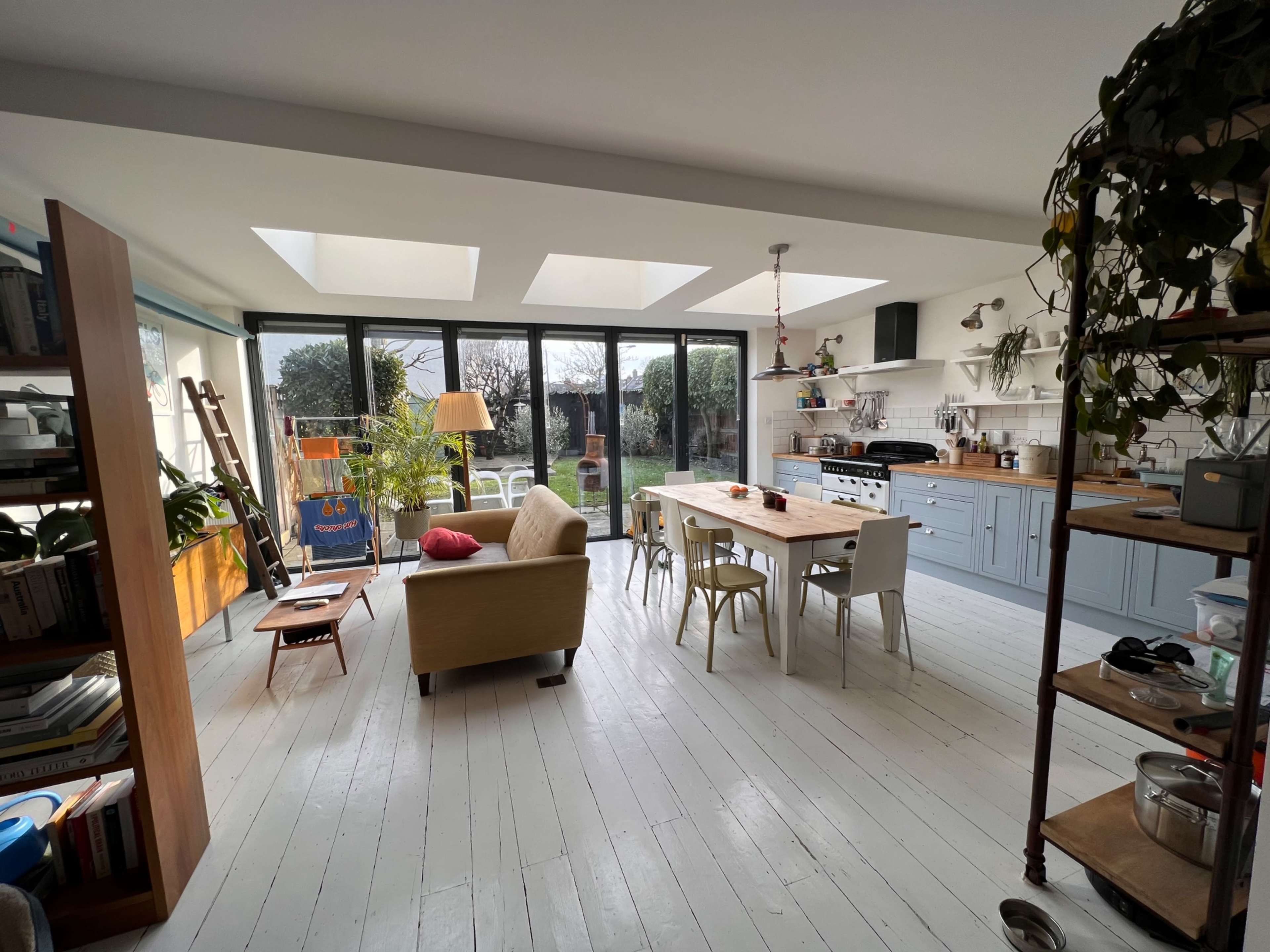 A bright kitchen and dining area features a large table, a seating area, and windows that overlook a garden.