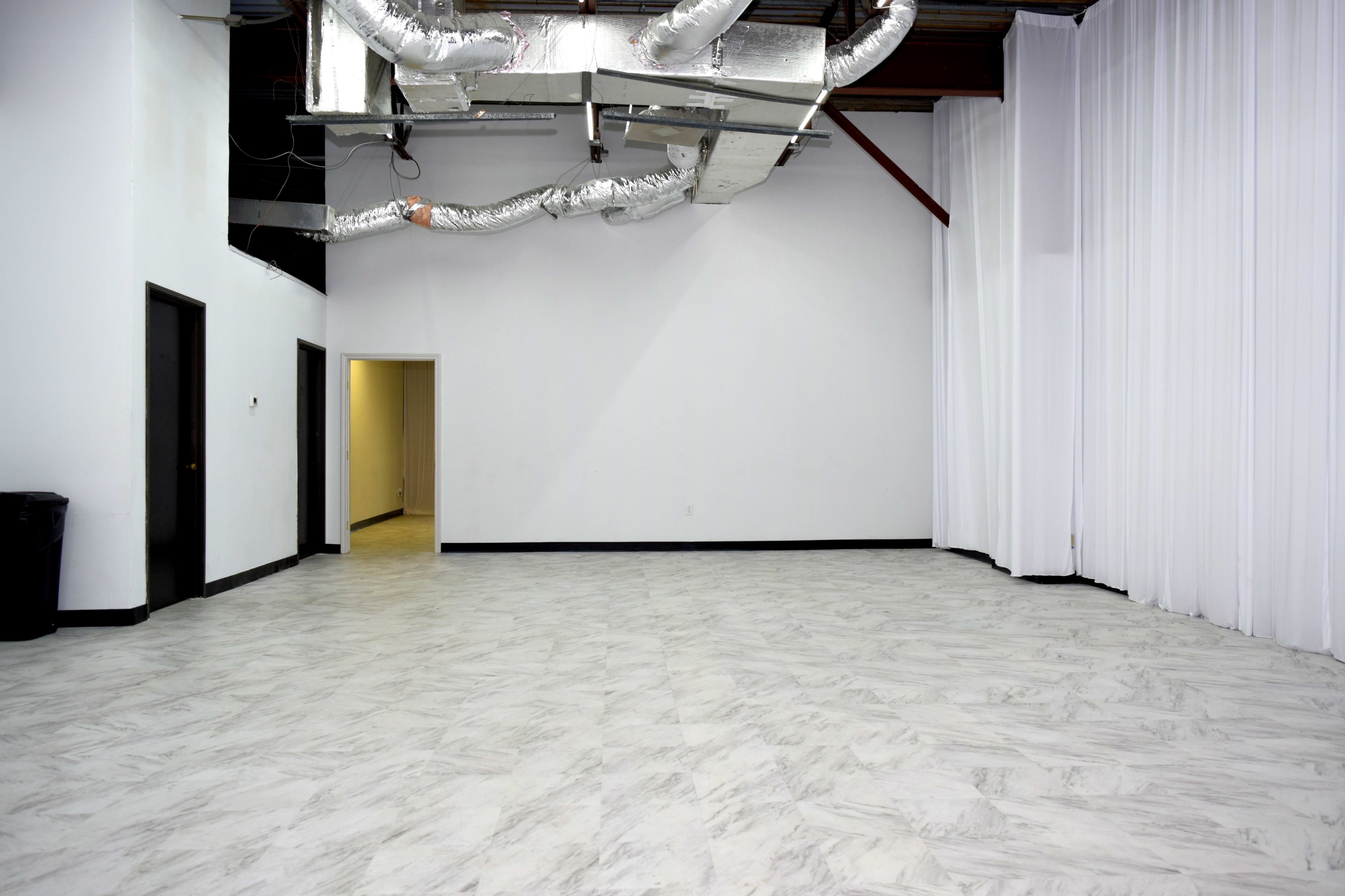 The image shows a spacious indoor area with white walls, a checkerboard floor, and visible air ducting on the ceiling.