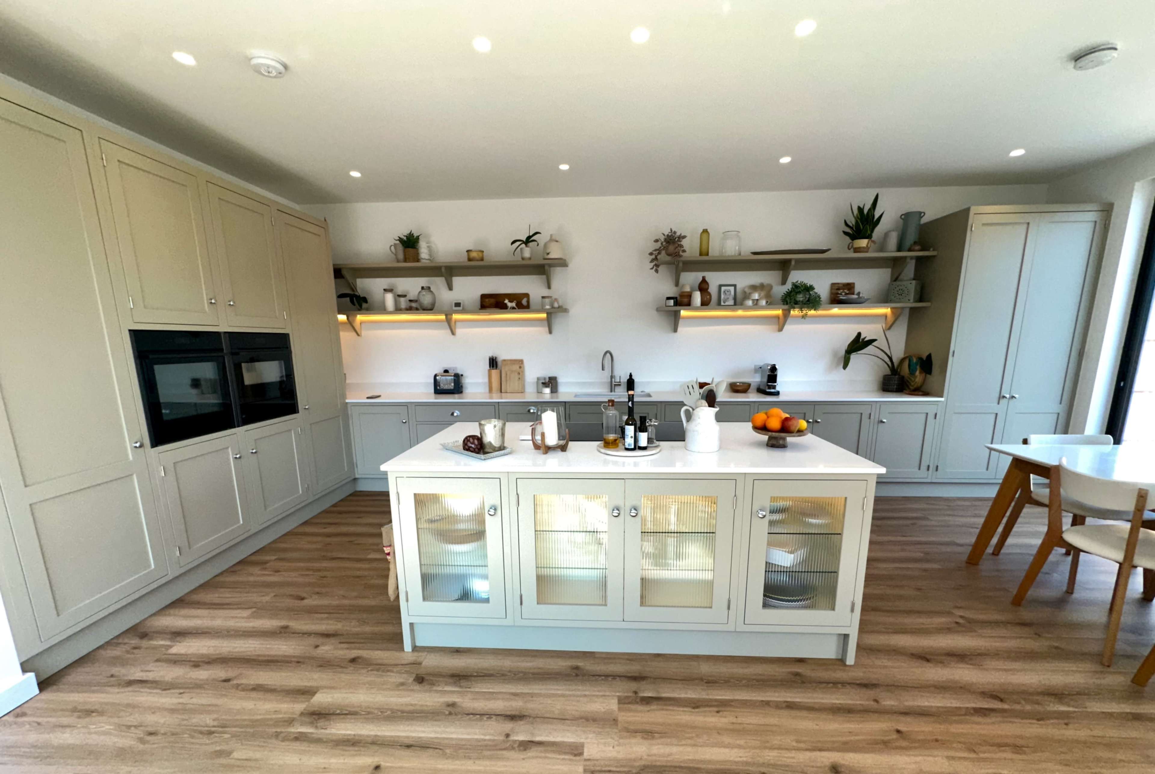 The image shows a modern kitchen with light cabinetry, an island with a white countertop, and wooden flooring.