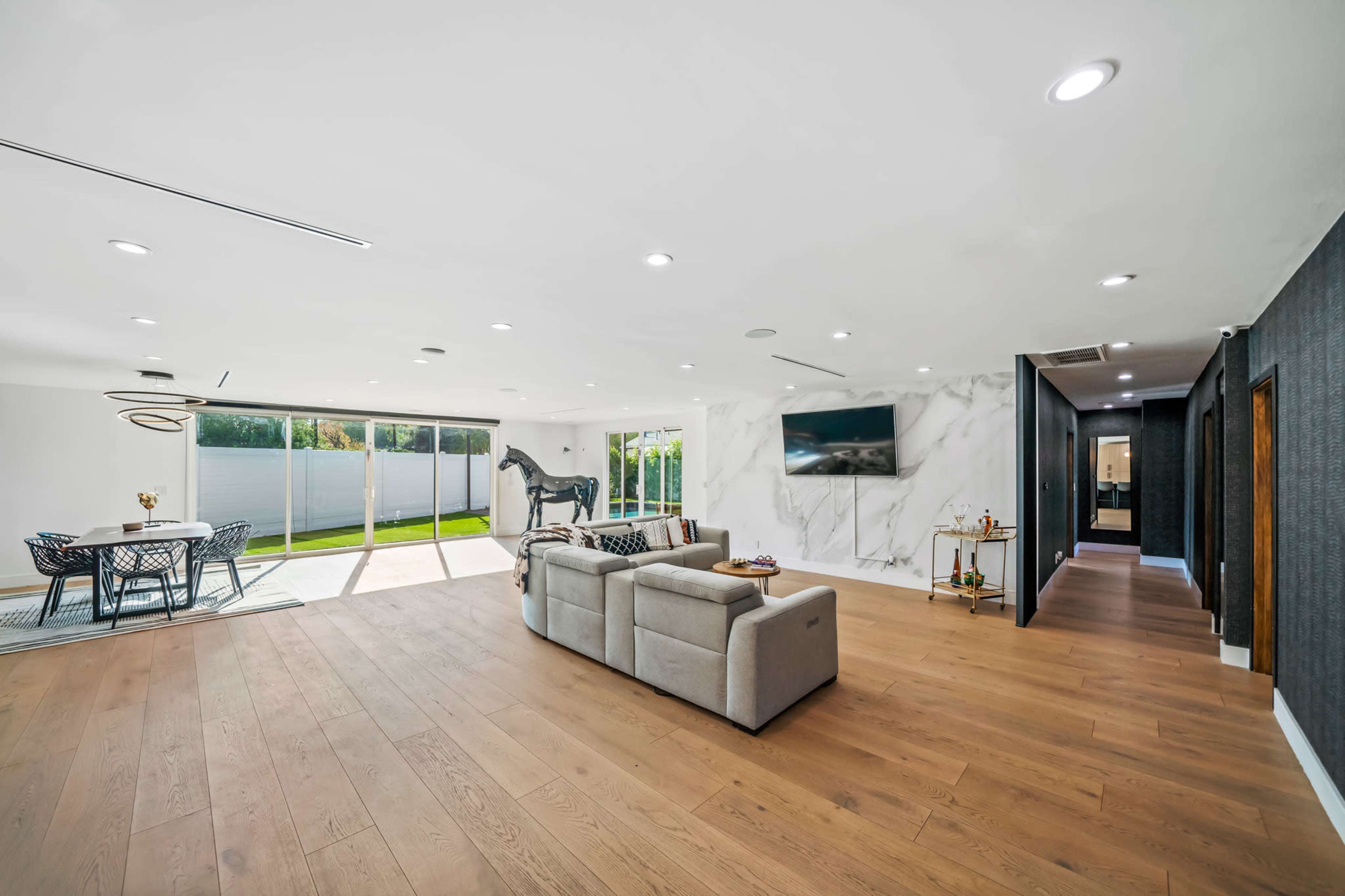 A modern living room with large windows overlooking a patio, a seating area with a light-colored sofa, and a wall featuring a large horse sculpture.