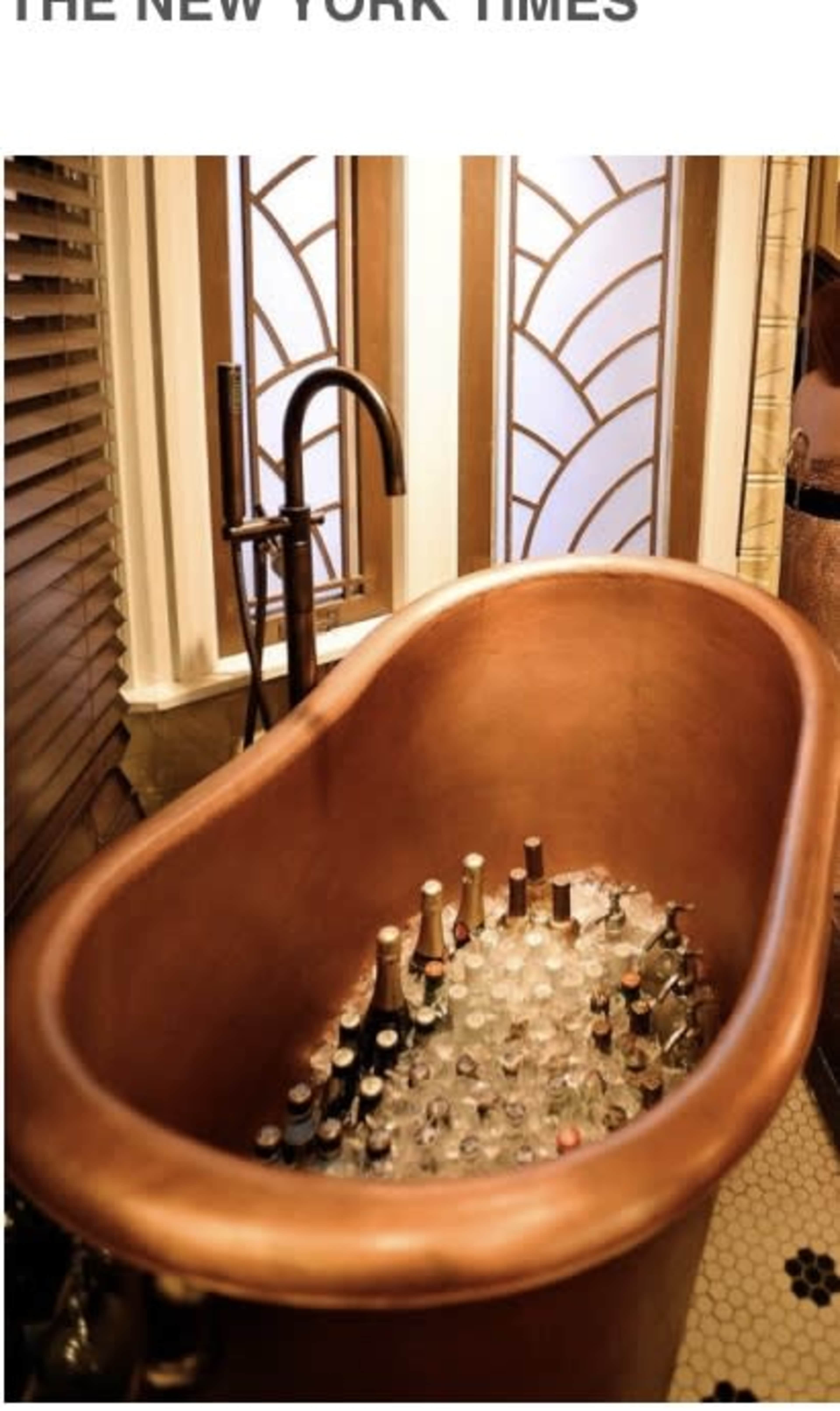 A vintage copper bathtub filled with ice and various bottles is set against a backdrop of decorative windows.