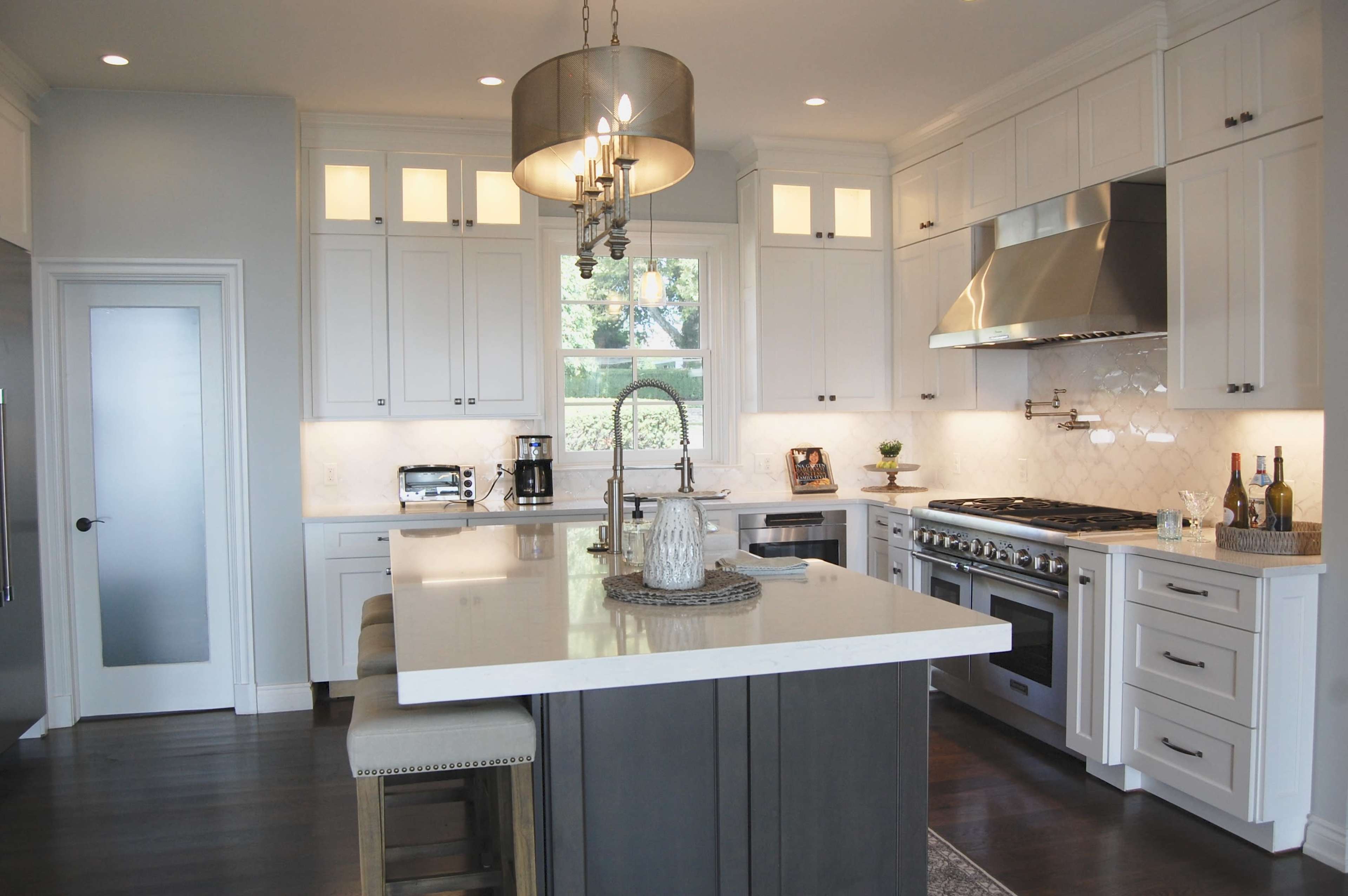 A modern kitchen features white cabinets, a large island with bar stools, stainless steel appliances, and a chandelier overhead.