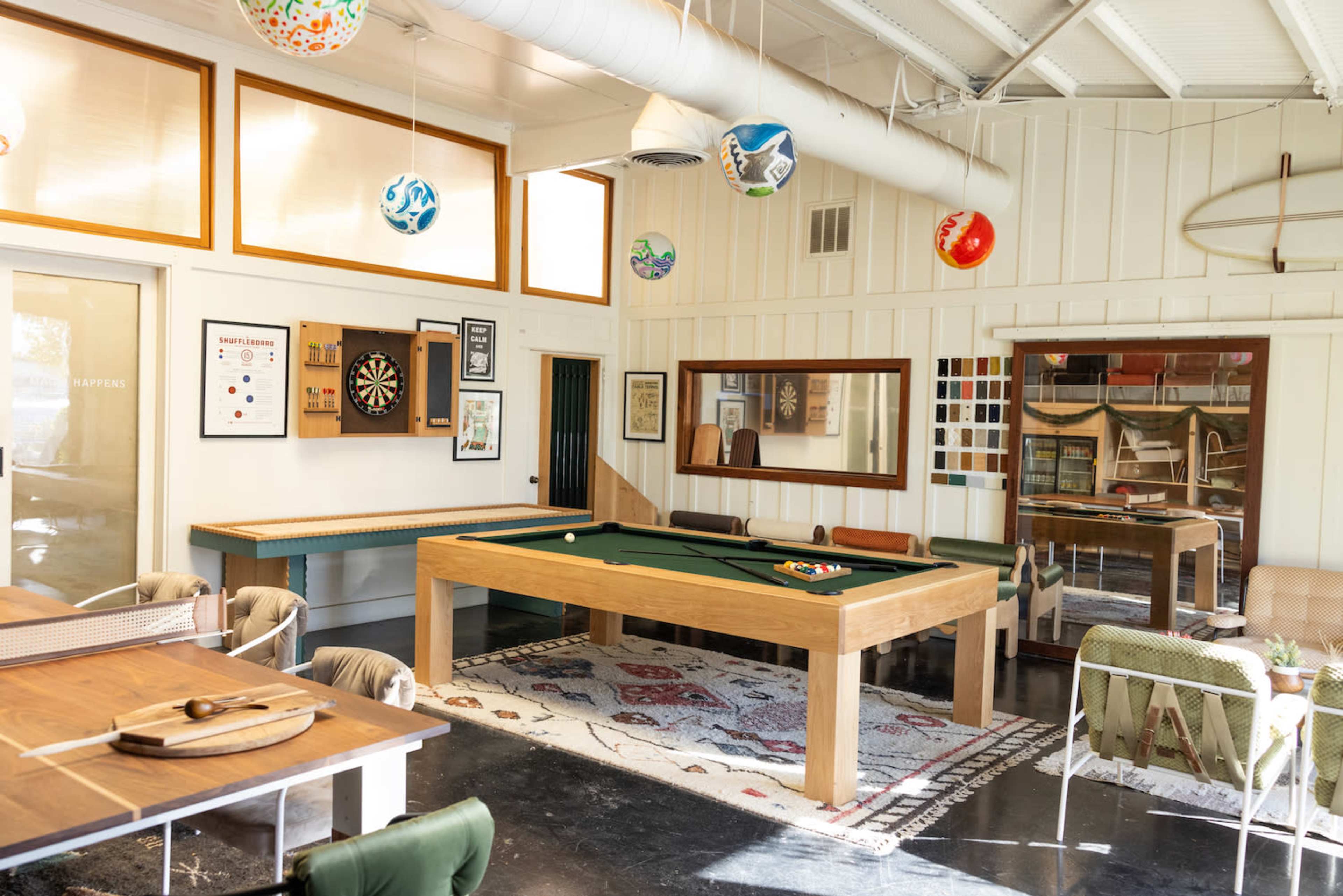 A recreational room featuring a pool table, dartboard, and various decorative elements on the walls, with a mix of seating arrangements and a large mirror.