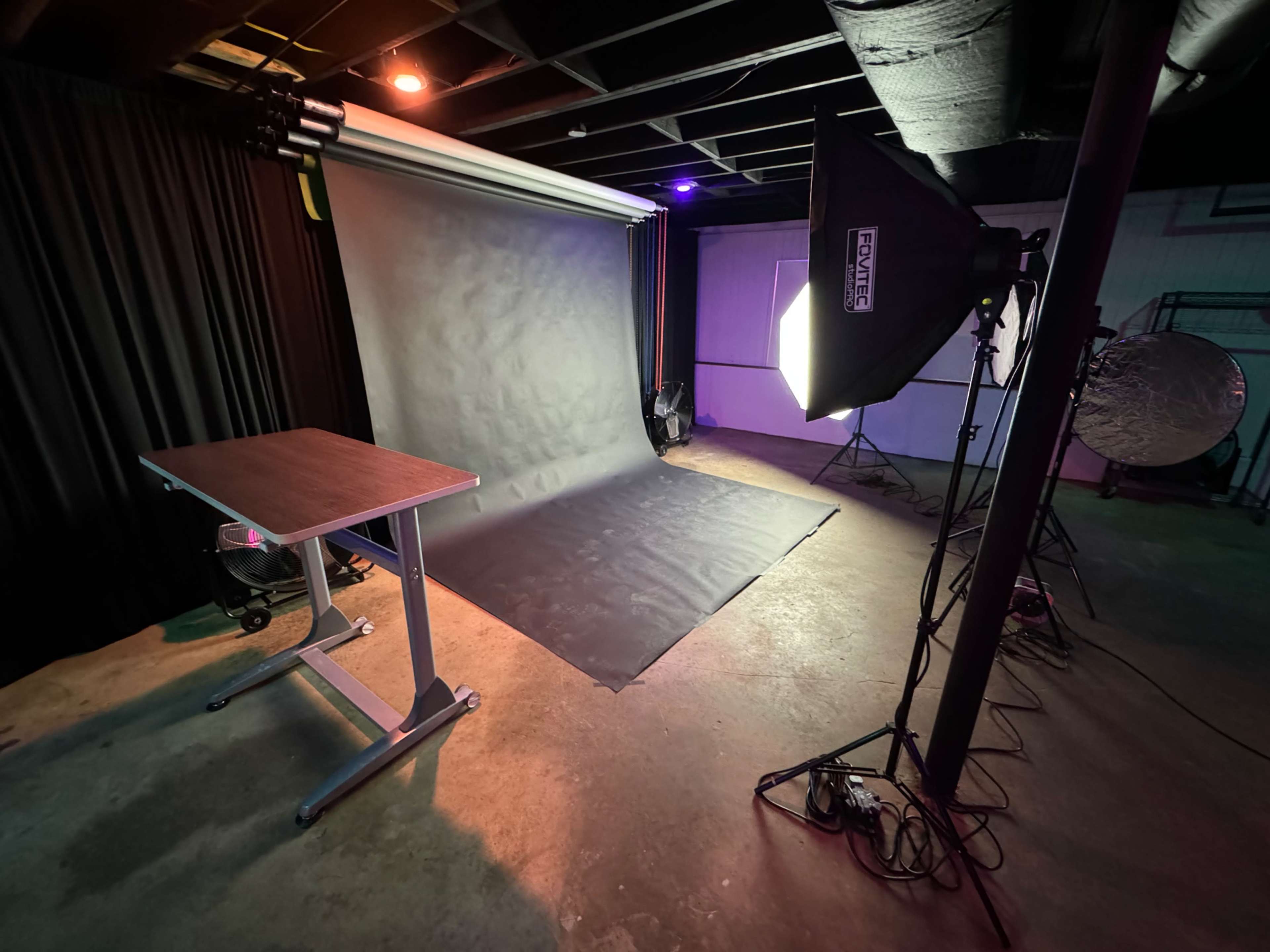 A photography studio setup featuring a backdrop, a table, and lighting equipment arranged on a concrete floor.