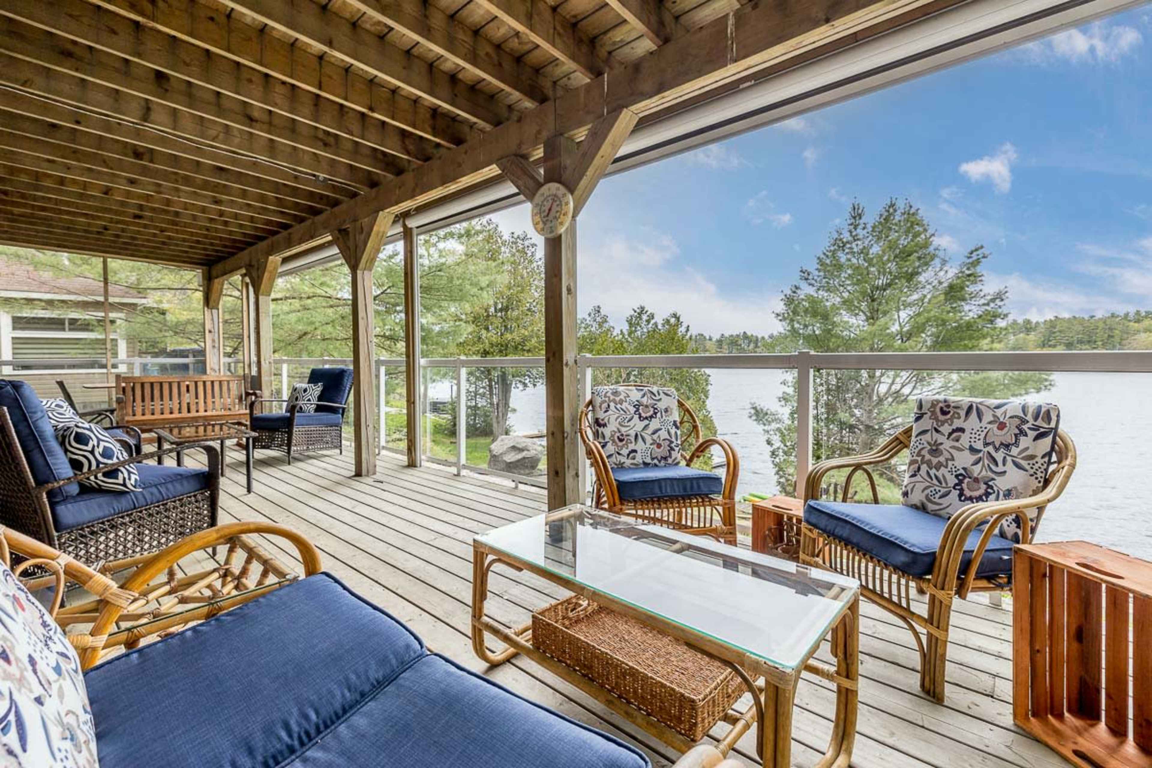 A wooden deck overlooking a lake, furnished with blue cushioned seating and a glass-topped coffee table.